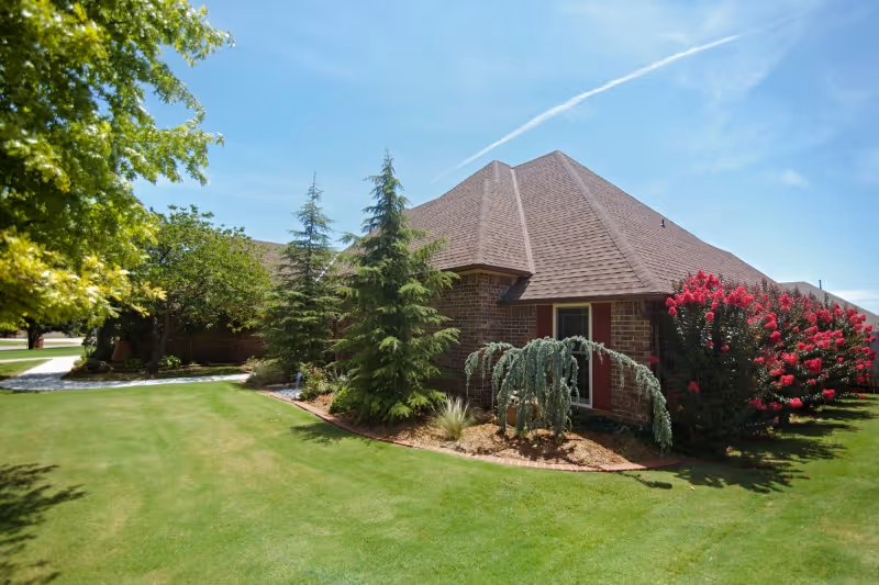Brick senior living facility exterior with manicured lawn and trees under blue sky