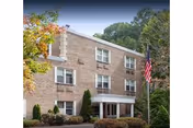 Brick senior living building with entrance, flagpole, and surrounding trees.