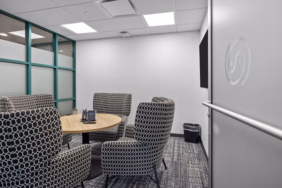 Interior meeting room with round table, patterned chairs, and glass partition.