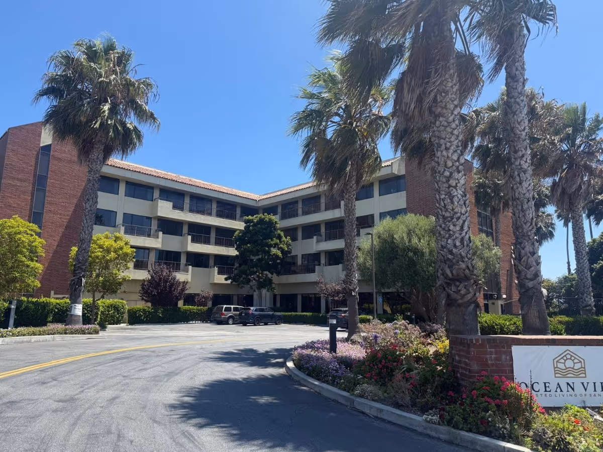 Exterior view of Serenity Senior Village building with palm trees and landscaped entrance.