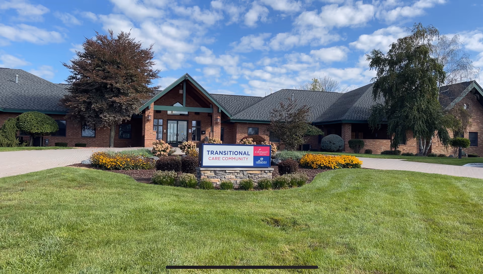 Brick single-story senior living facility front with a landscaped lawn and a sign reading 'Transitional Care Community'.