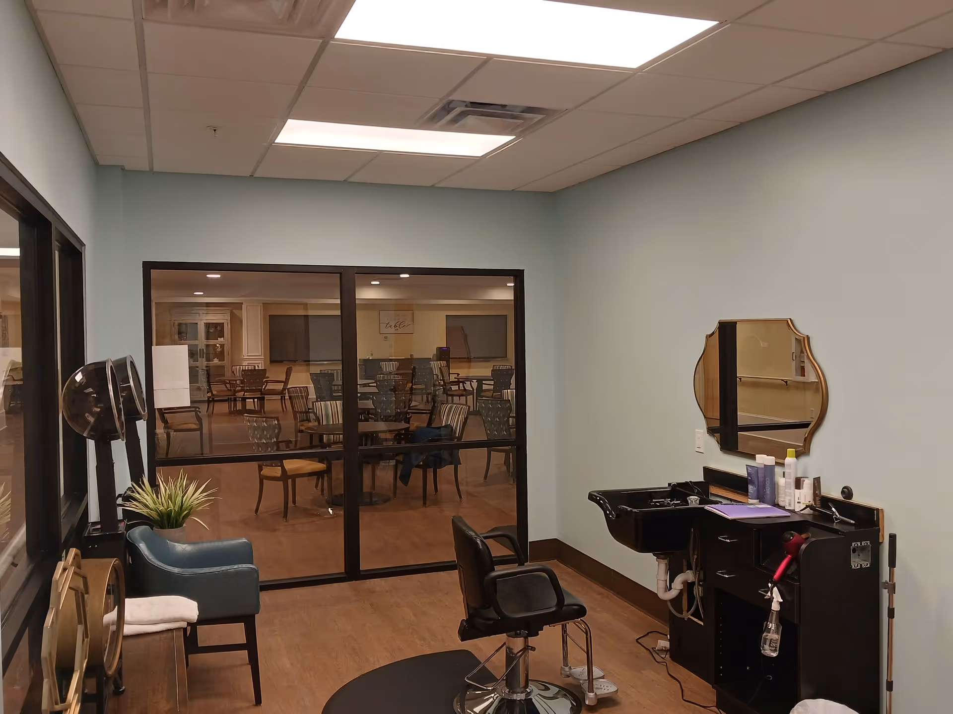 Salon styling station with mirror and chair, facing a dining area through glass doors.