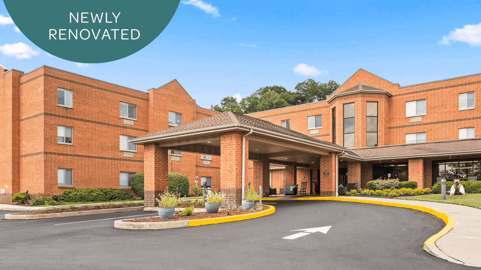 Brick senior living facility exterior with curved driveway and covered entrance, new renovation banner.