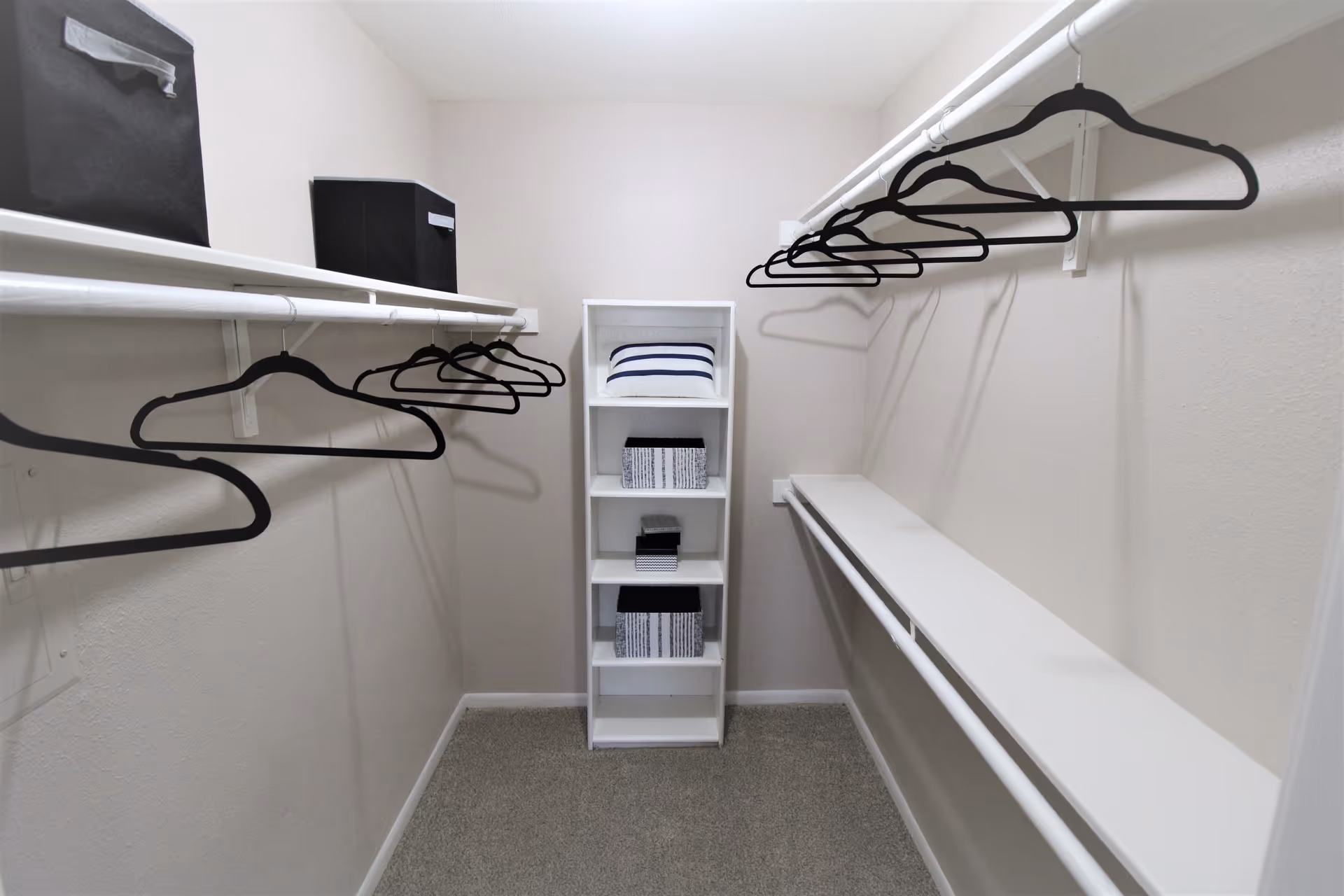 Bright walk-in closet with rods, shelves, and stacked storage boxes along white walls.