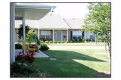 Front exterior of a single-story senior living building with a green lawn and walkway.