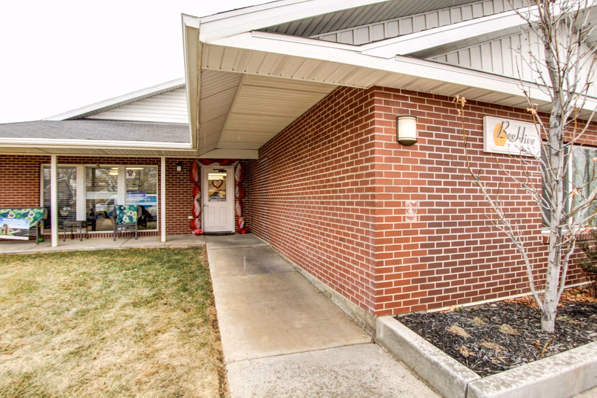 Front entrance of a brick senior living building with a covered walkway, windows and a 'Beehive' sign.