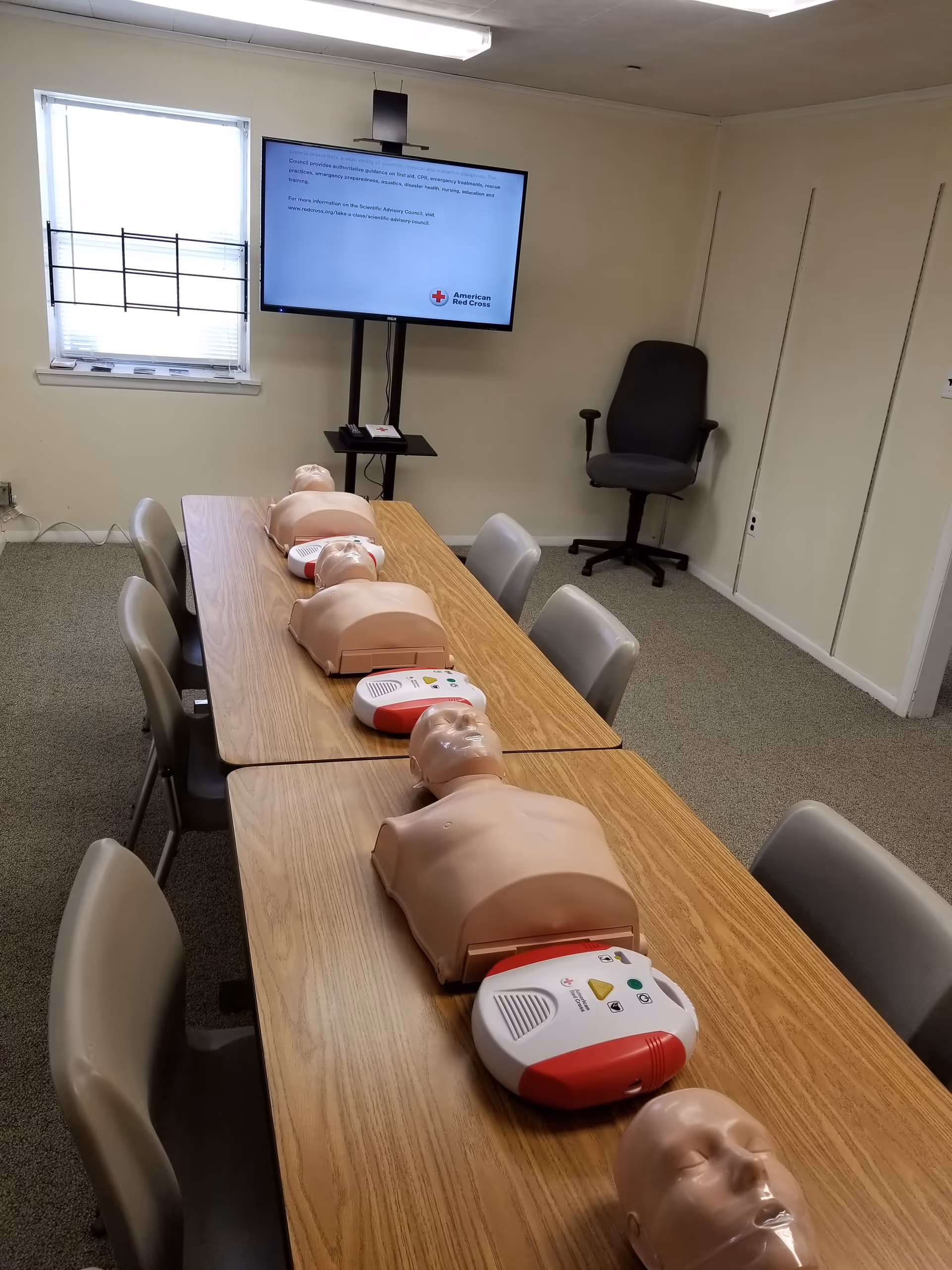 CPR training room with multiple mannequins on a long table and monitor.