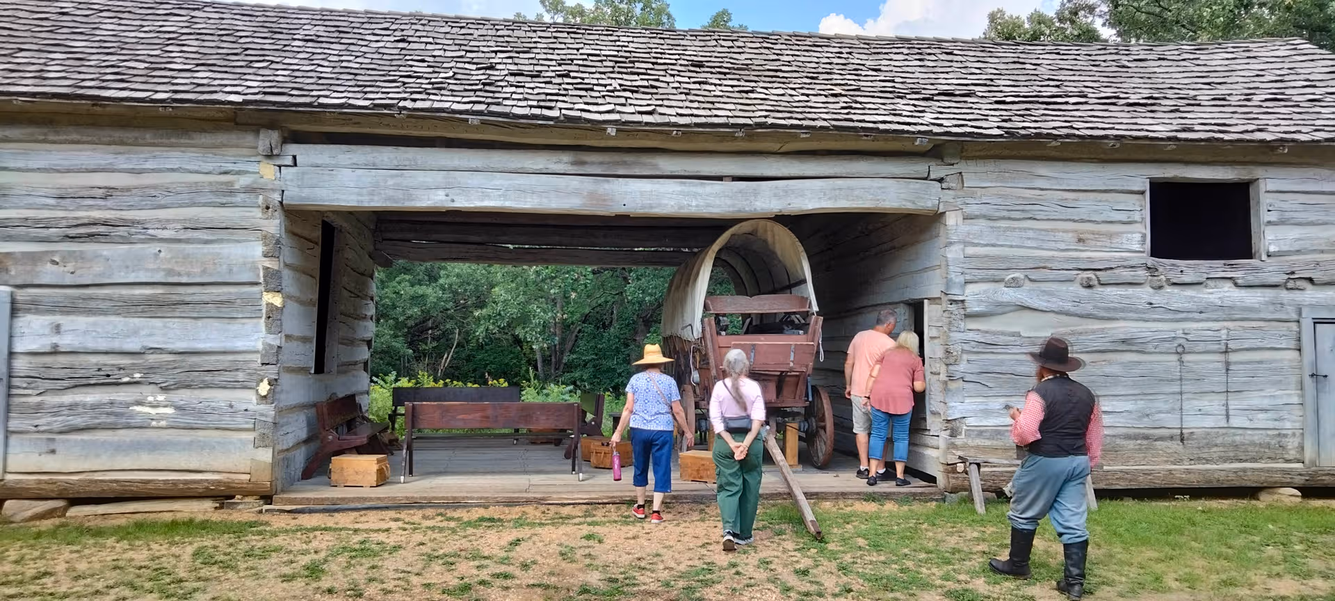 Group of people outside a weathered wooden barn with a wagon wheel.