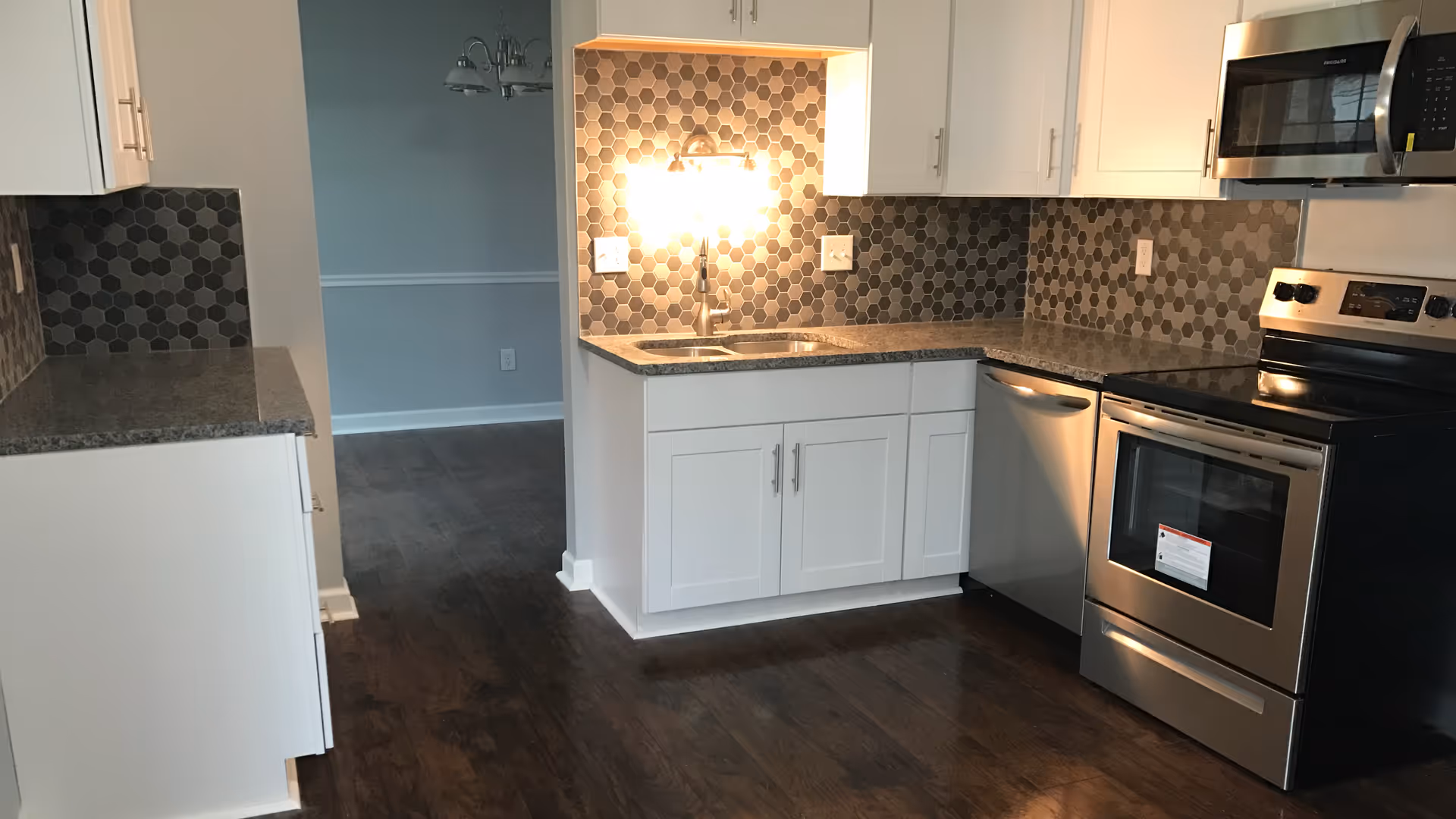 Modern kitchen with white cabinets, dark countertops, hex tile backsplash, and stainless appliances.
