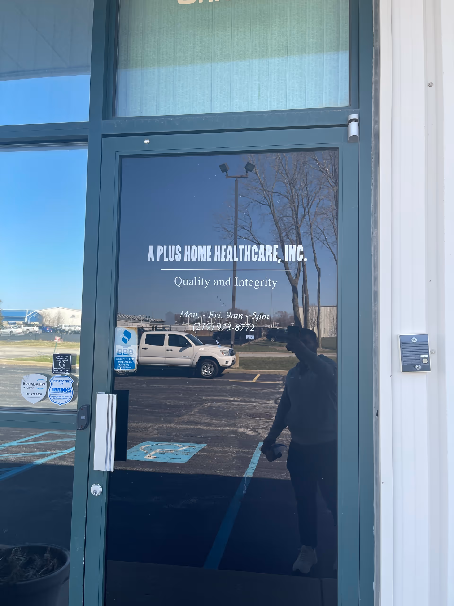 Glass entrance door for A Plus Home Health Care, Inc., reflecting parking lot and trees.