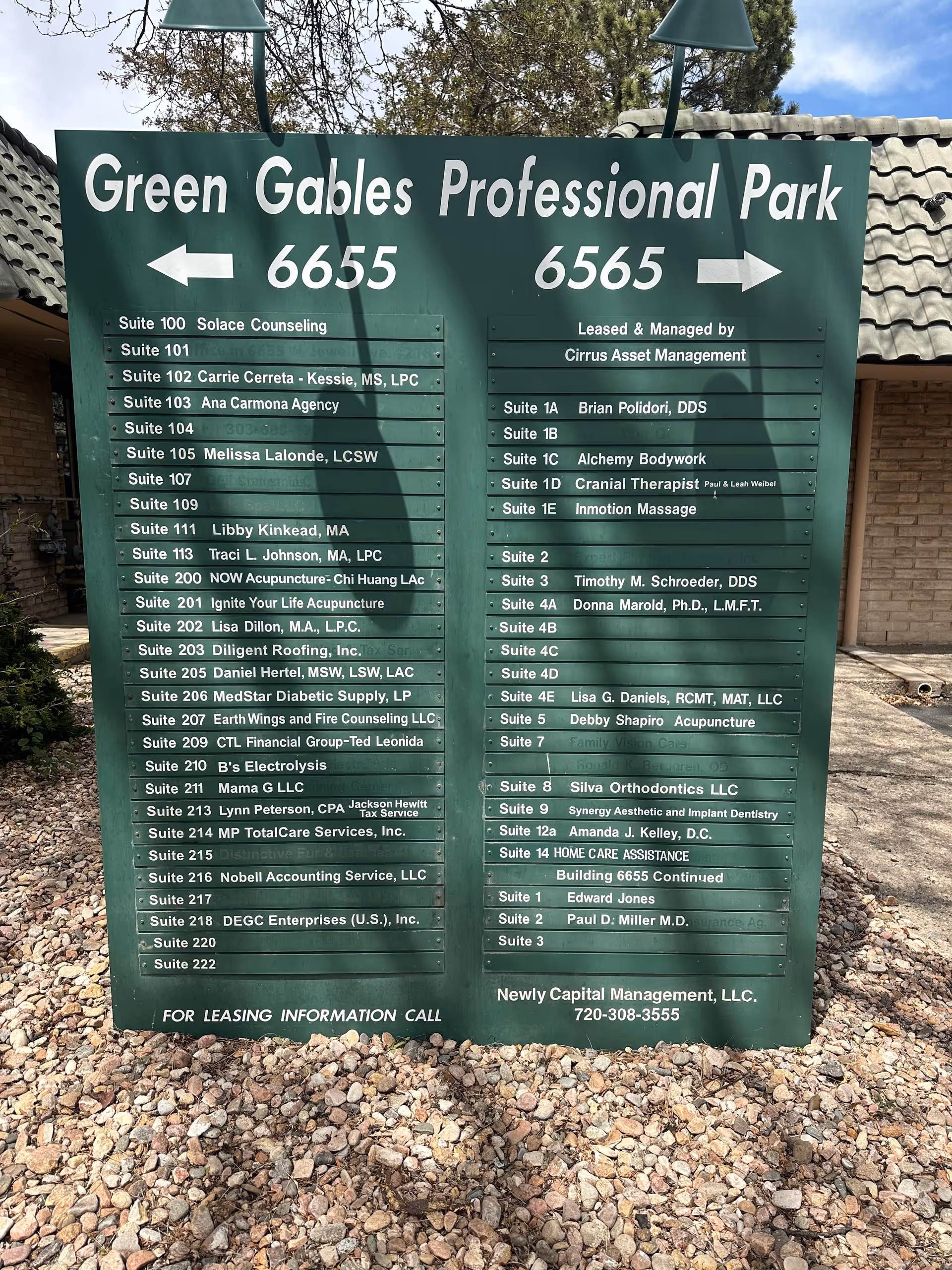 Large green outdoor signboard listing suites at Green Gables Professional Park, with rocky ground.