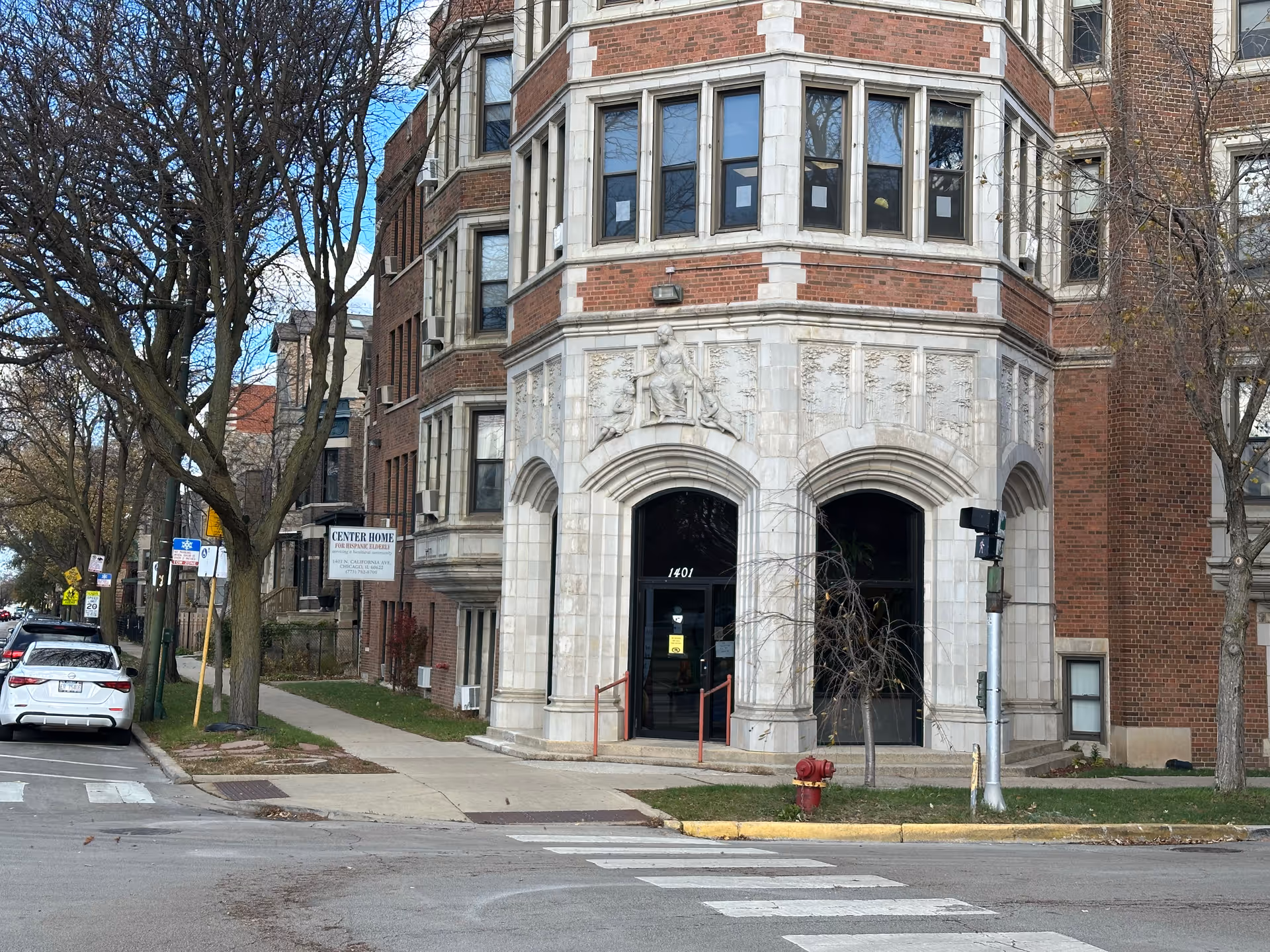 Front entrance of a multi-story brick building with ornate stone arches, a sidewalk sign reading "Center Home", and a crosswalk in the foreground.