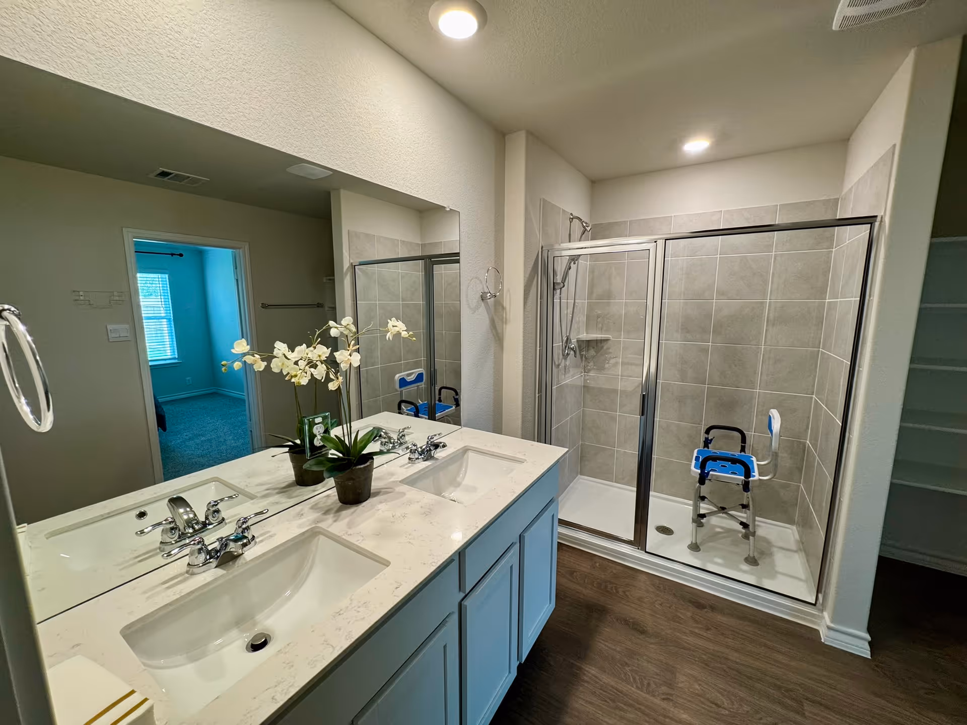 Double-sink bathroom with glass shower enclosure, vanity mirrors, and a shower chair.