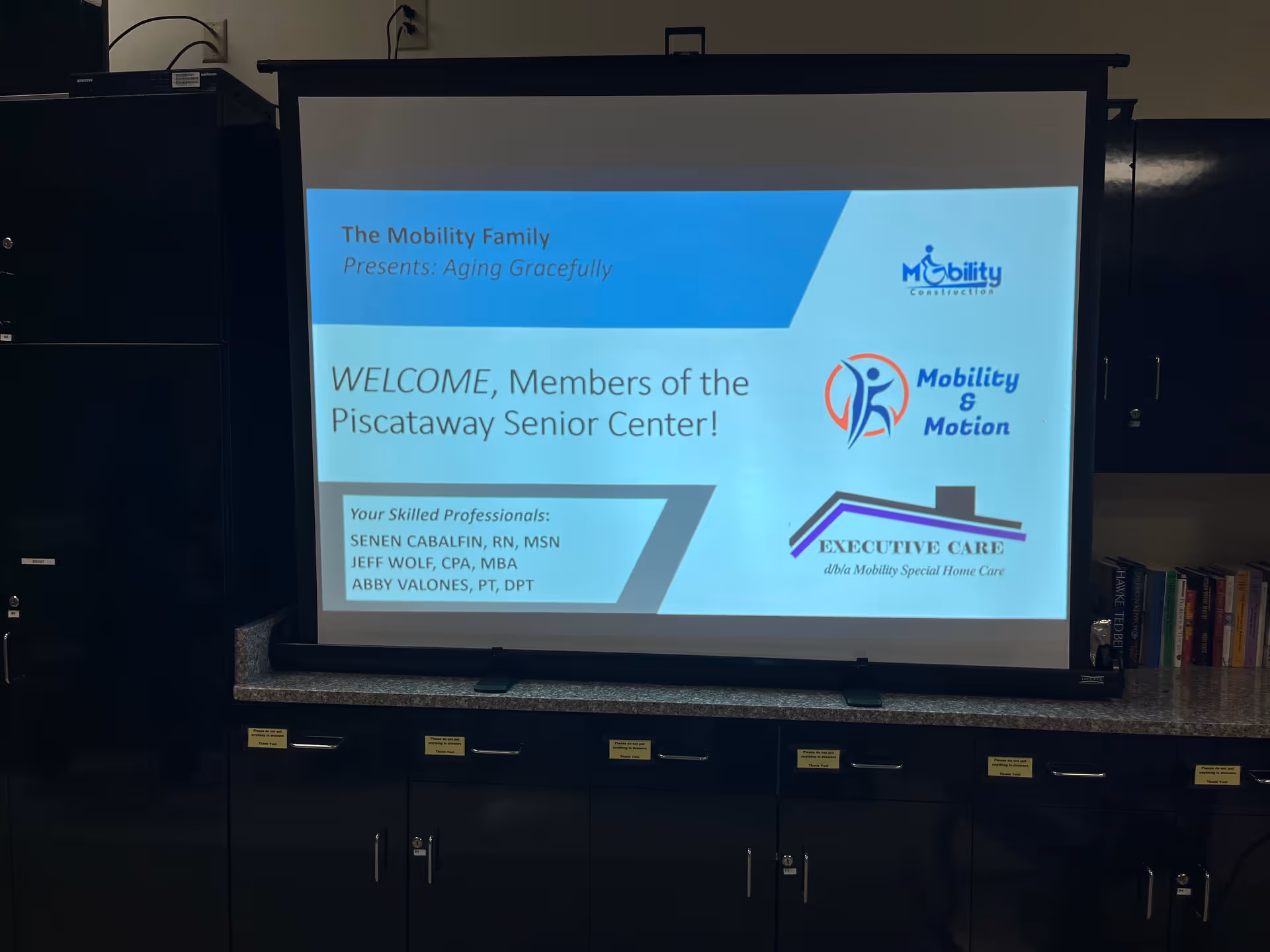 Projection screen displays welcome message and logos for Mobility & Motion LLC in a conference room.