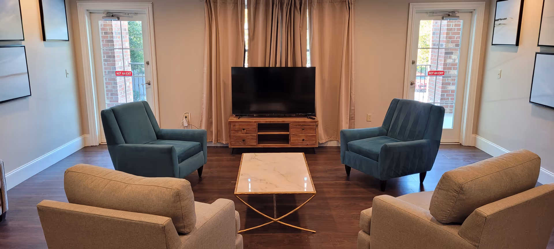 A modern facility living room with teal chairs, a marble coffee table, and TV.