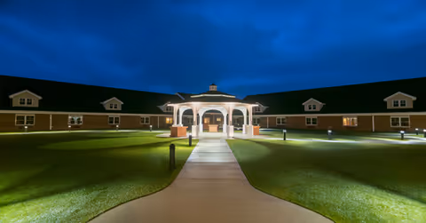 Nighttime exterior view of Armstrong Memory Care Assisted Living with a lit central entrance and walkway.
