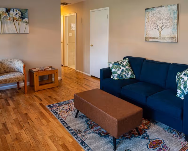 Cozy senior living room featuring blue sofa, coffee table, rug, and wall art.