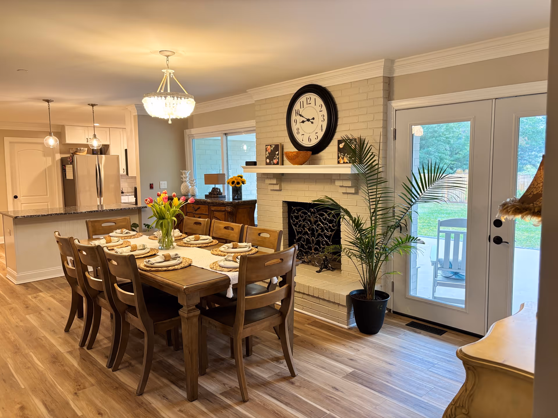 A spacious dining room with a long wooden table, chairs, chandelier, and a fireplace.