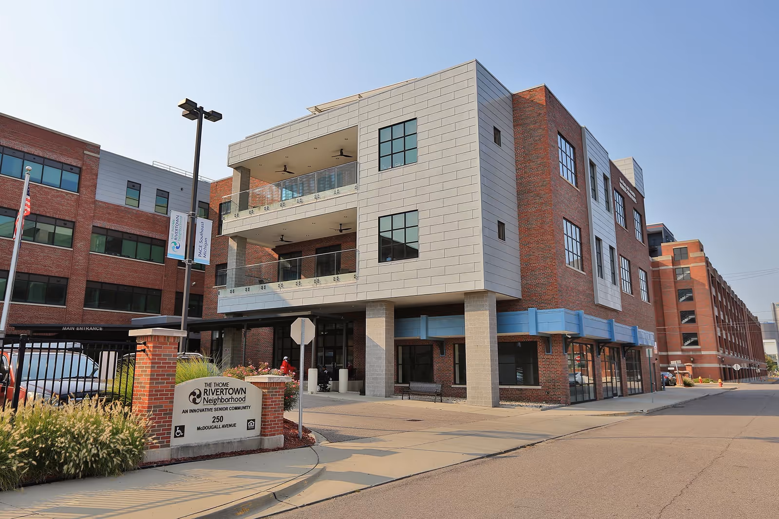Exterior view of a multi-story brick and metal-clad senior living building with balconies and an entrance sign for The Thome Rivertown Neighborhood.