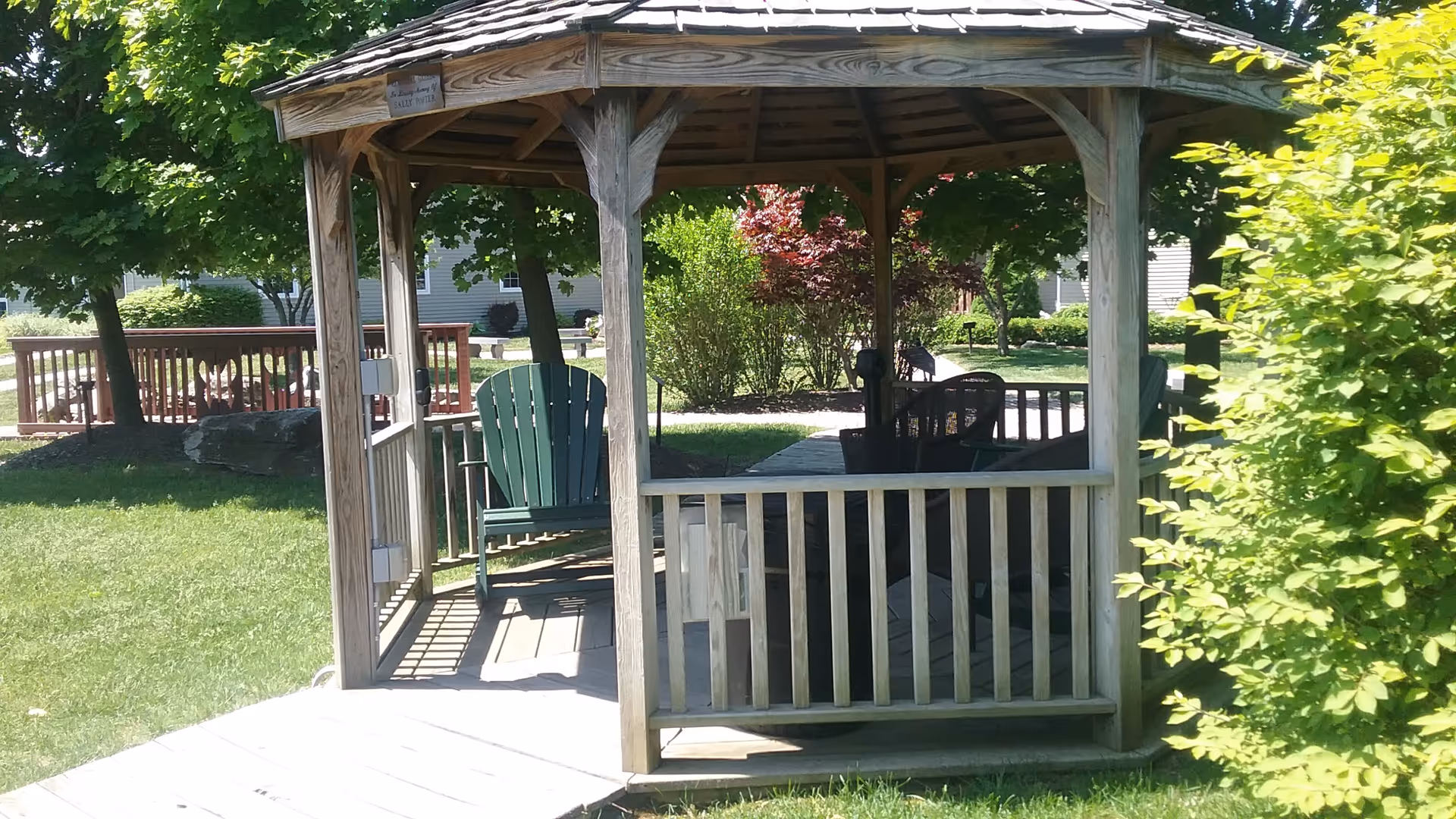 Wooden gazebo with seating sits in a sunny, landscaped courtyard.