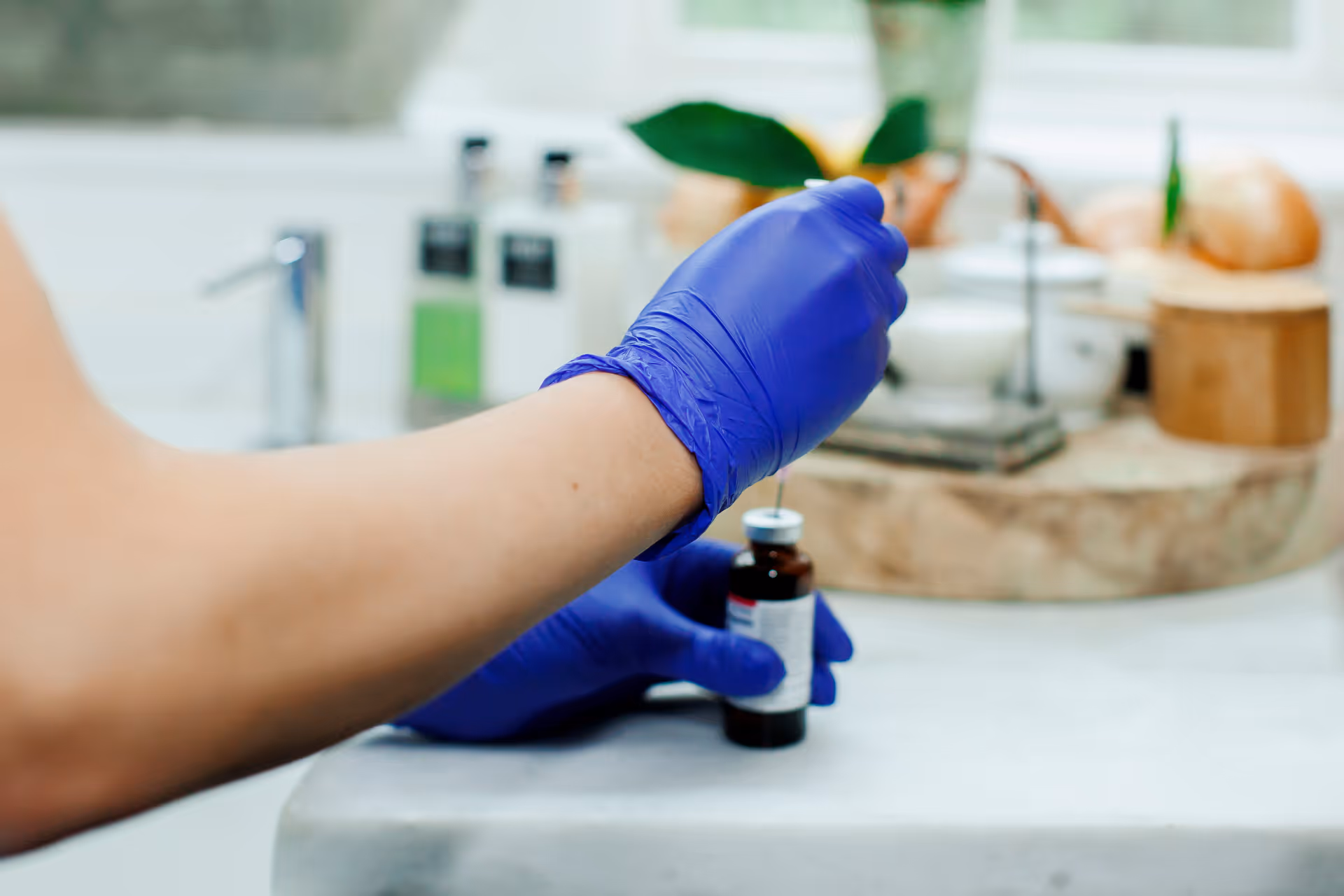 Gloved hands prepare a syringe beside a medication bottle on a kitchen counter.