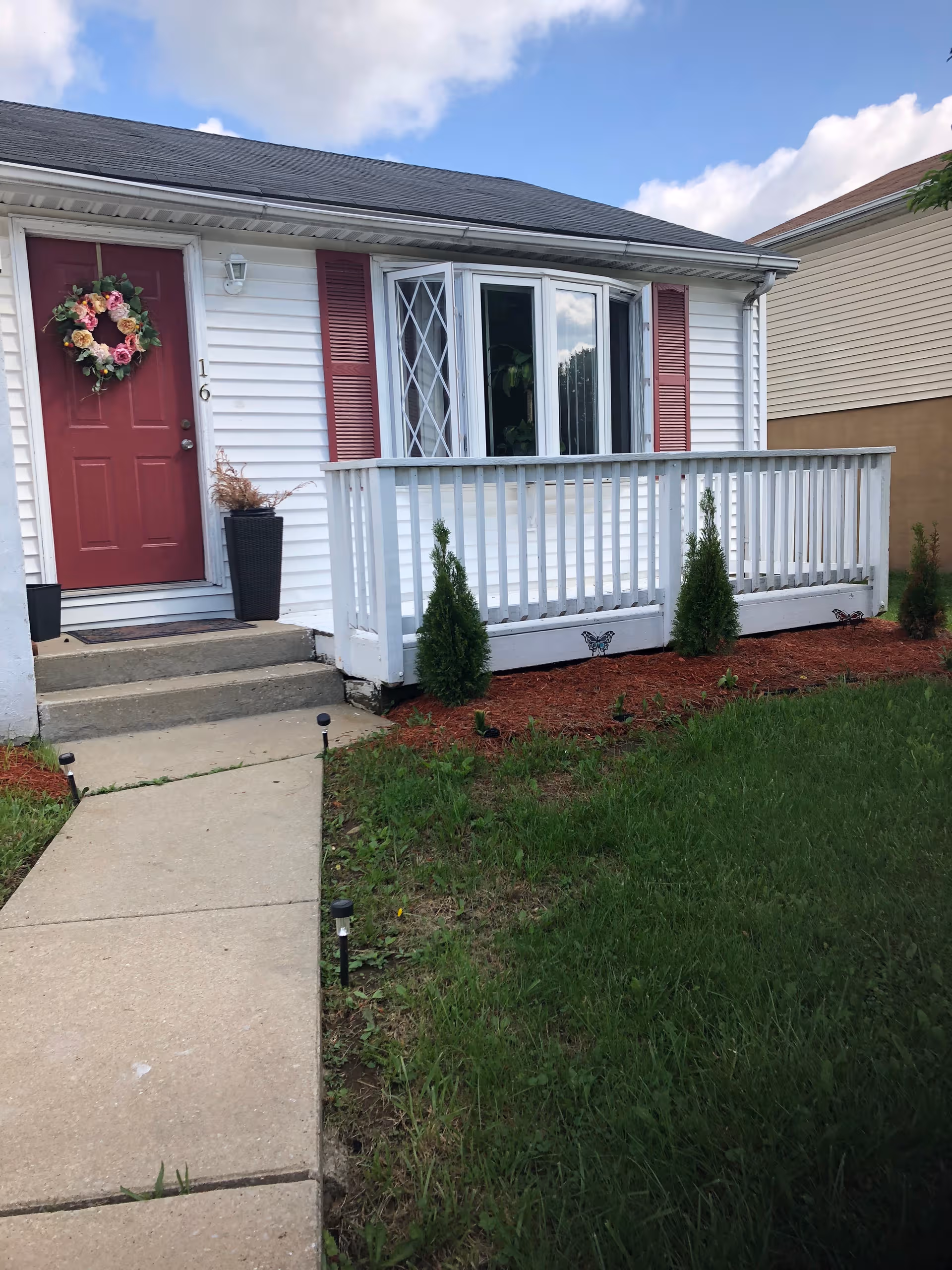 White one-story home with red front door and wreath on small porch.