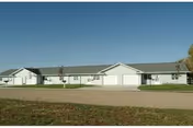 Single-story senior living facility with light siding and a long driveway in front.