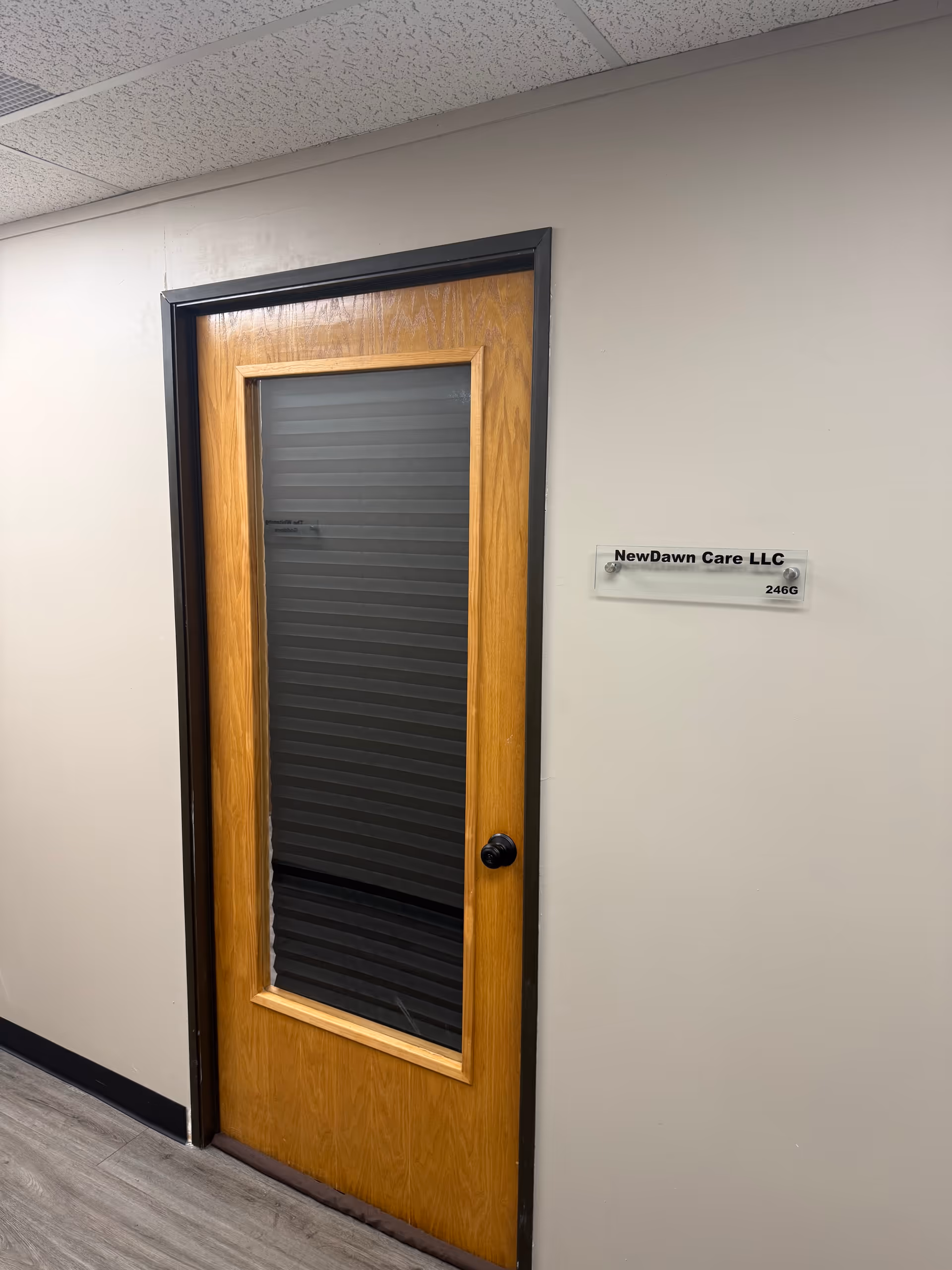 Wooden door with glass panel in a hallway; sign reads NewDawn Care LLC.