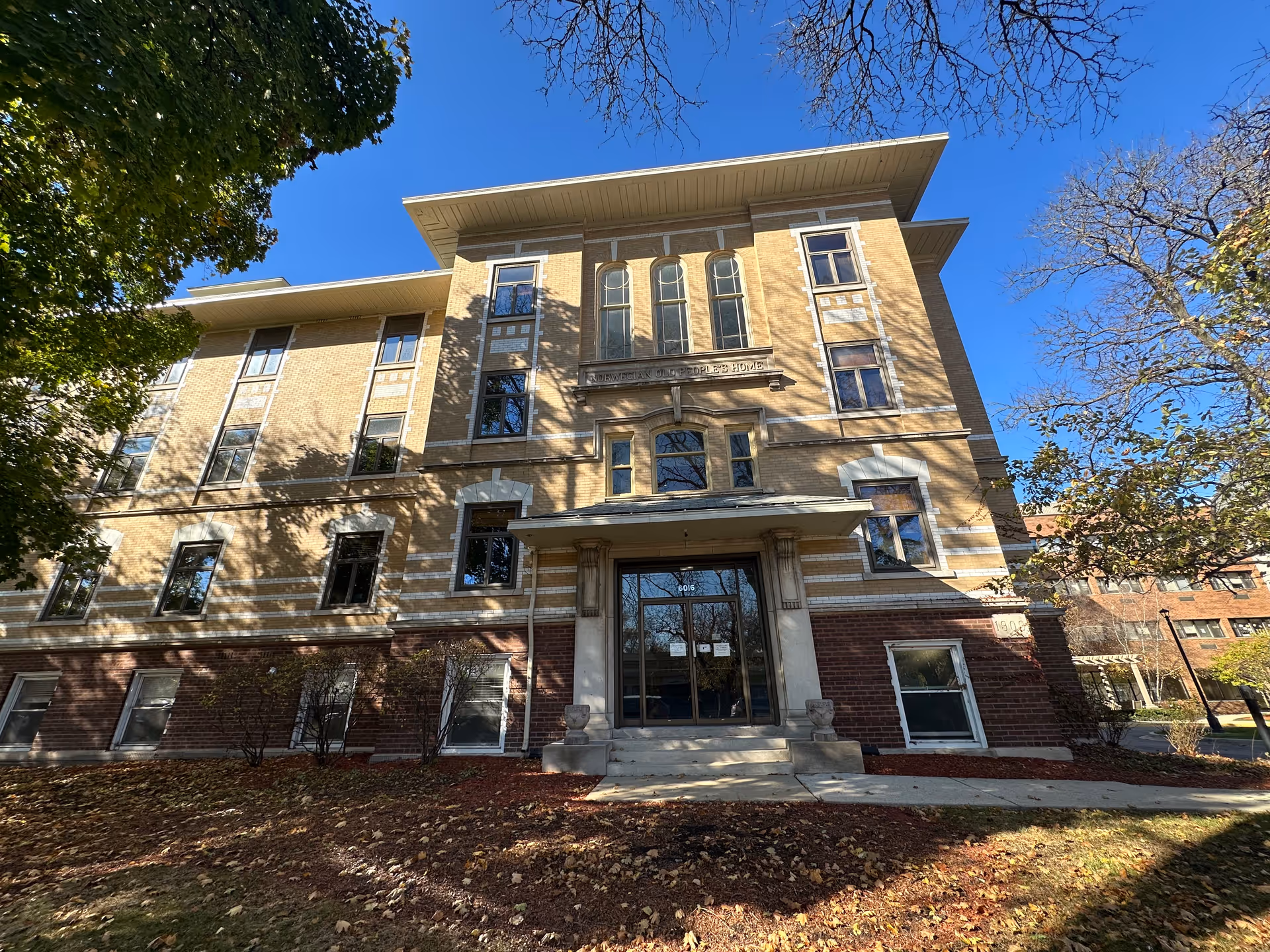 Front entrance of a historic multi-story brick and stone building with steps and trees against a clear blue sky.