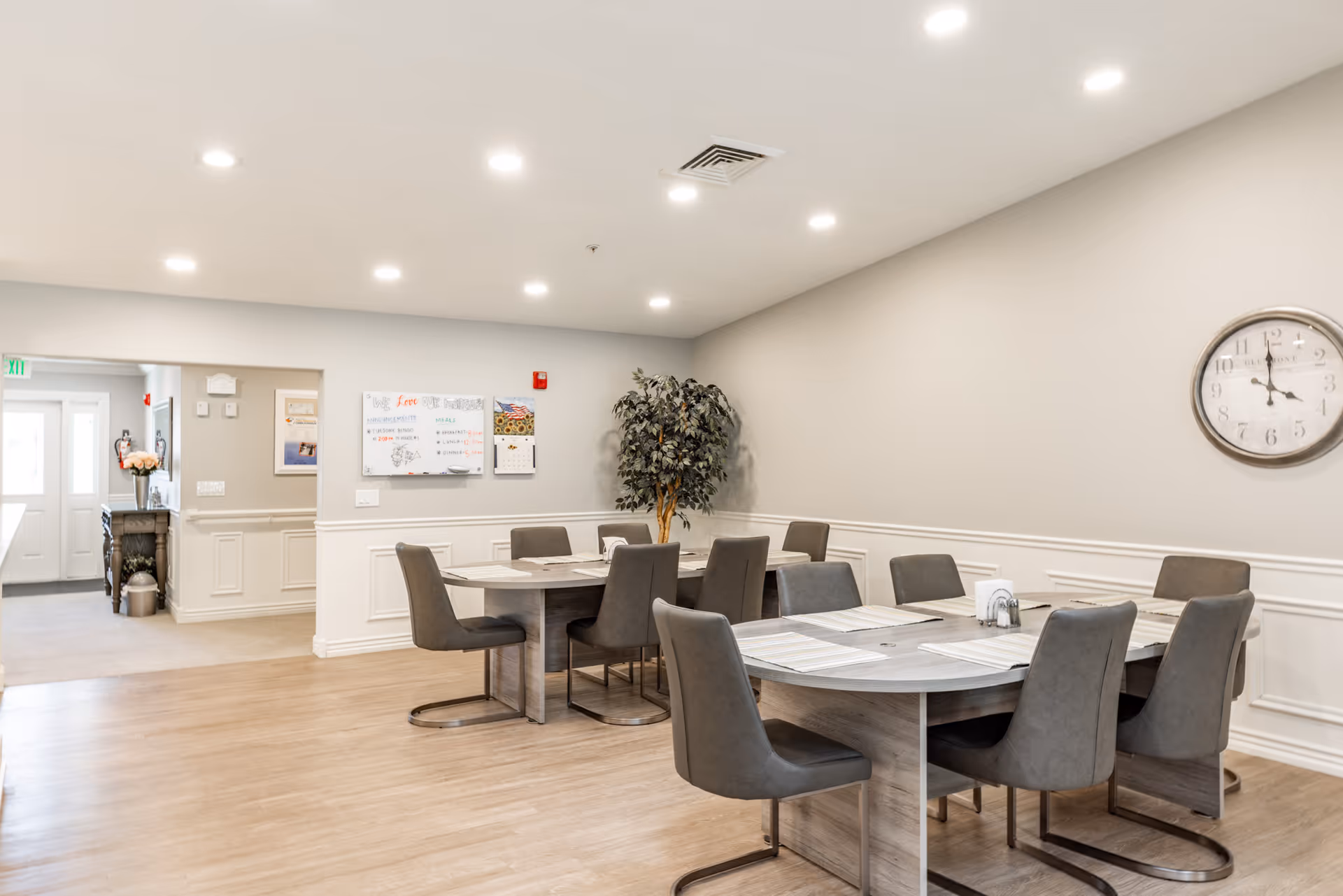 Bright dining area with round tables, gray chairs, and wall clock in Country Care II.