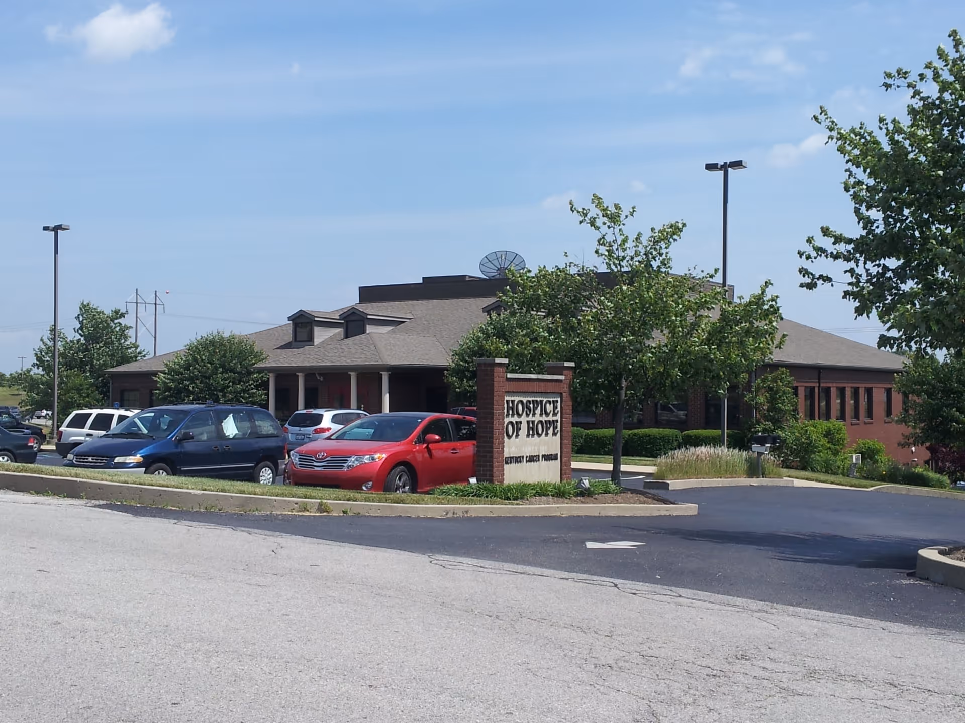 Exterior view of Hospice of Hope facility with brick building, trees, and parked cars.