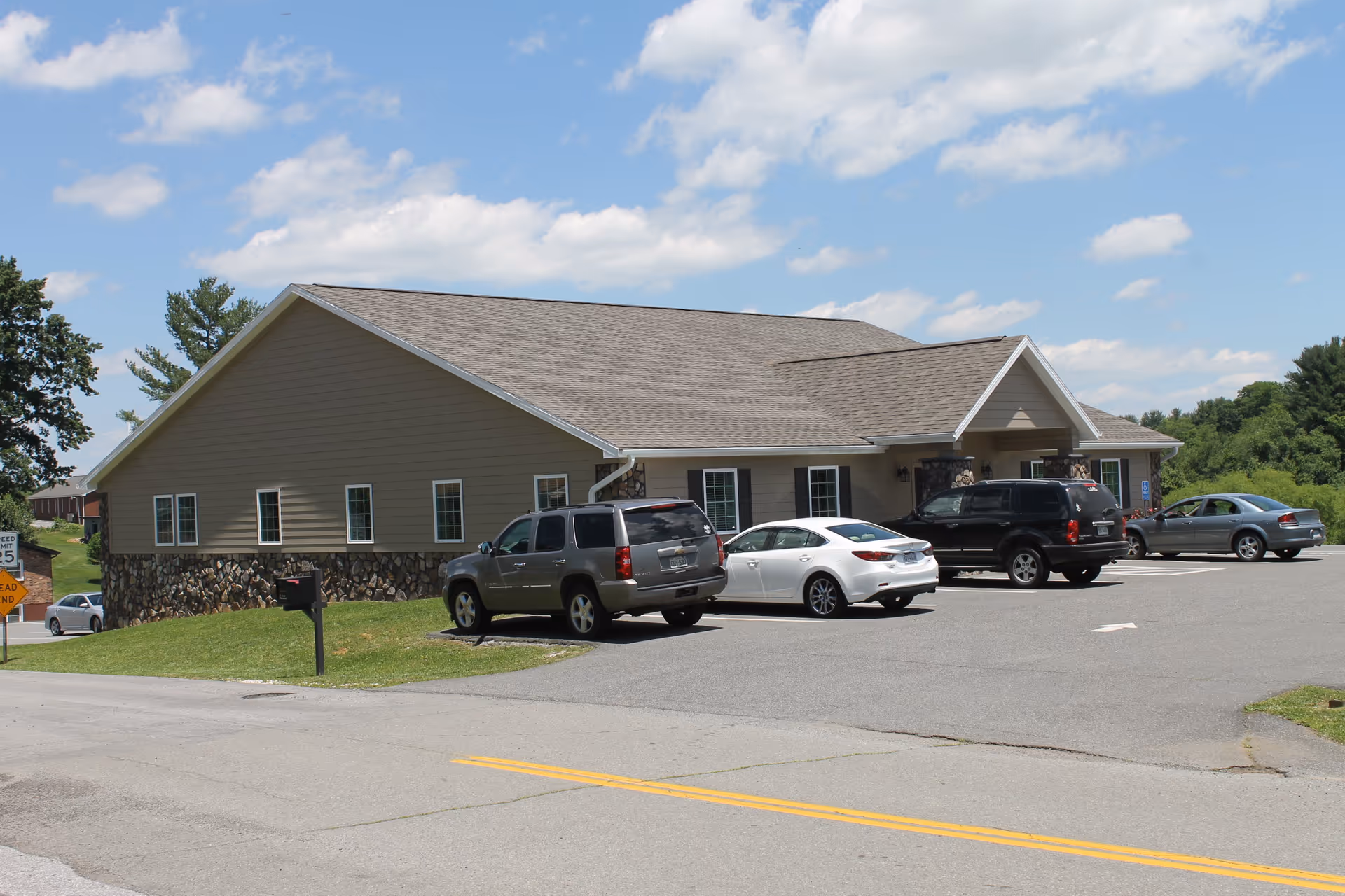 A single-story senior living facility with a stone base and parked cars in front.