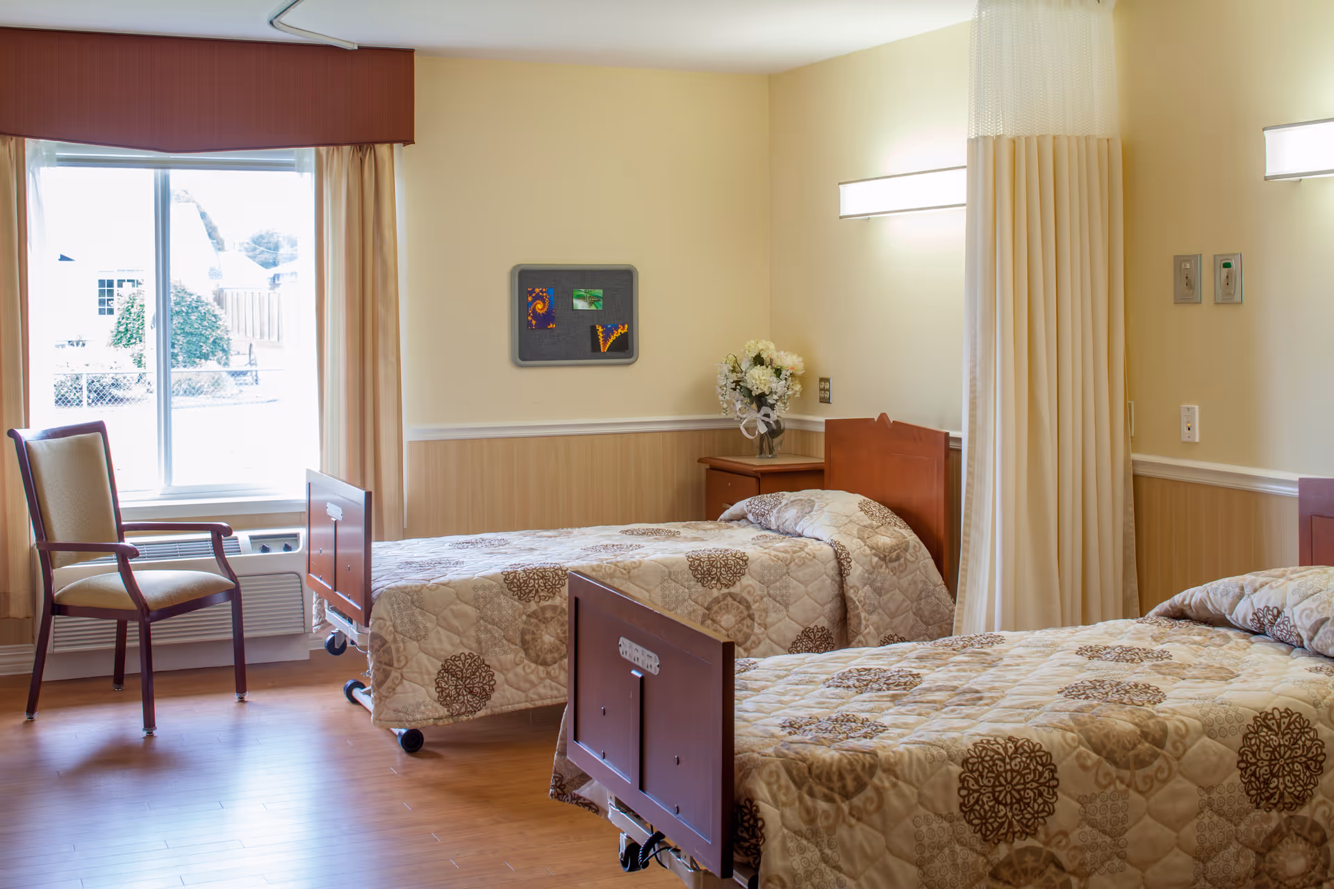 Two single beds with patterned quilts in a bright shared senior living bedroom.