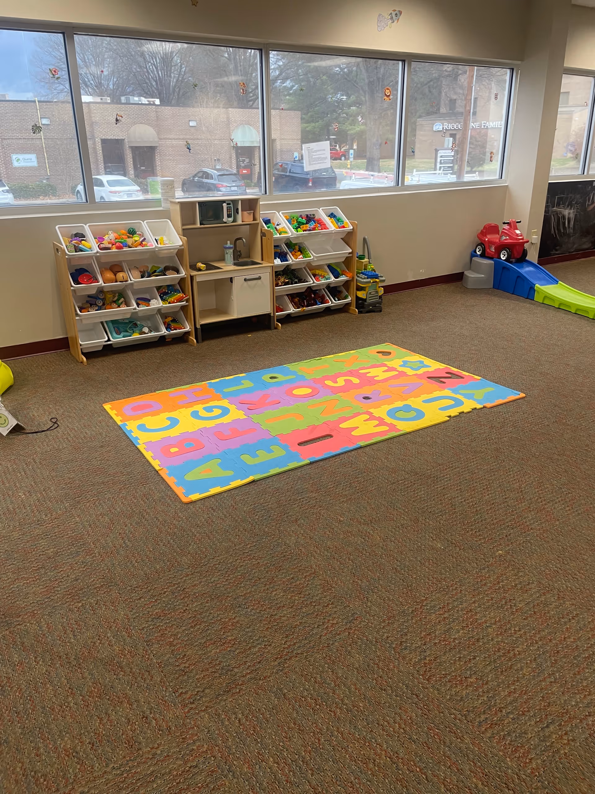 Colorful children's play area with toy shelves, alphabet mat, and a slide inside a facility.