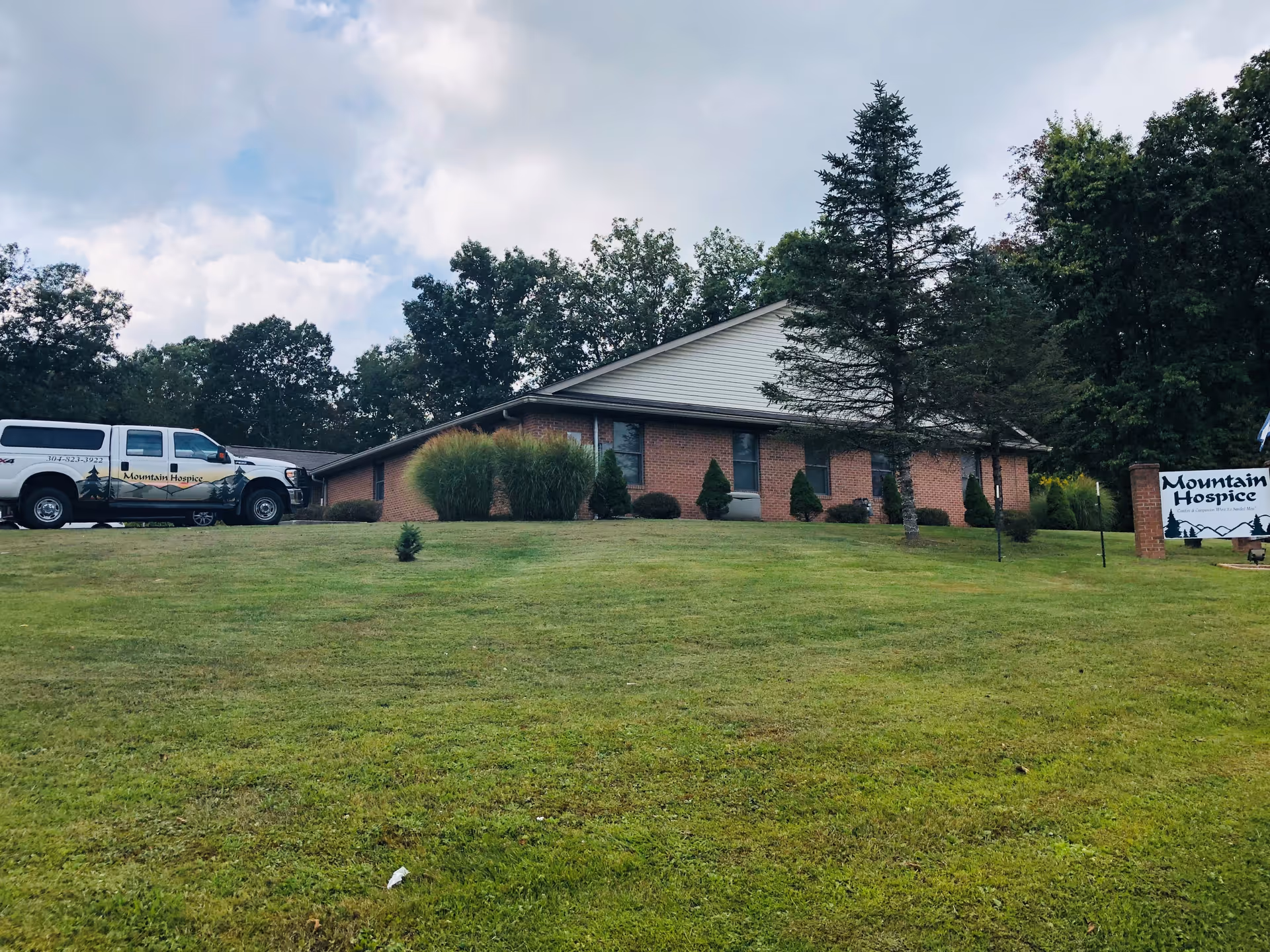 Single-story brick hospice building with manicured lawn and a white van parked nearby