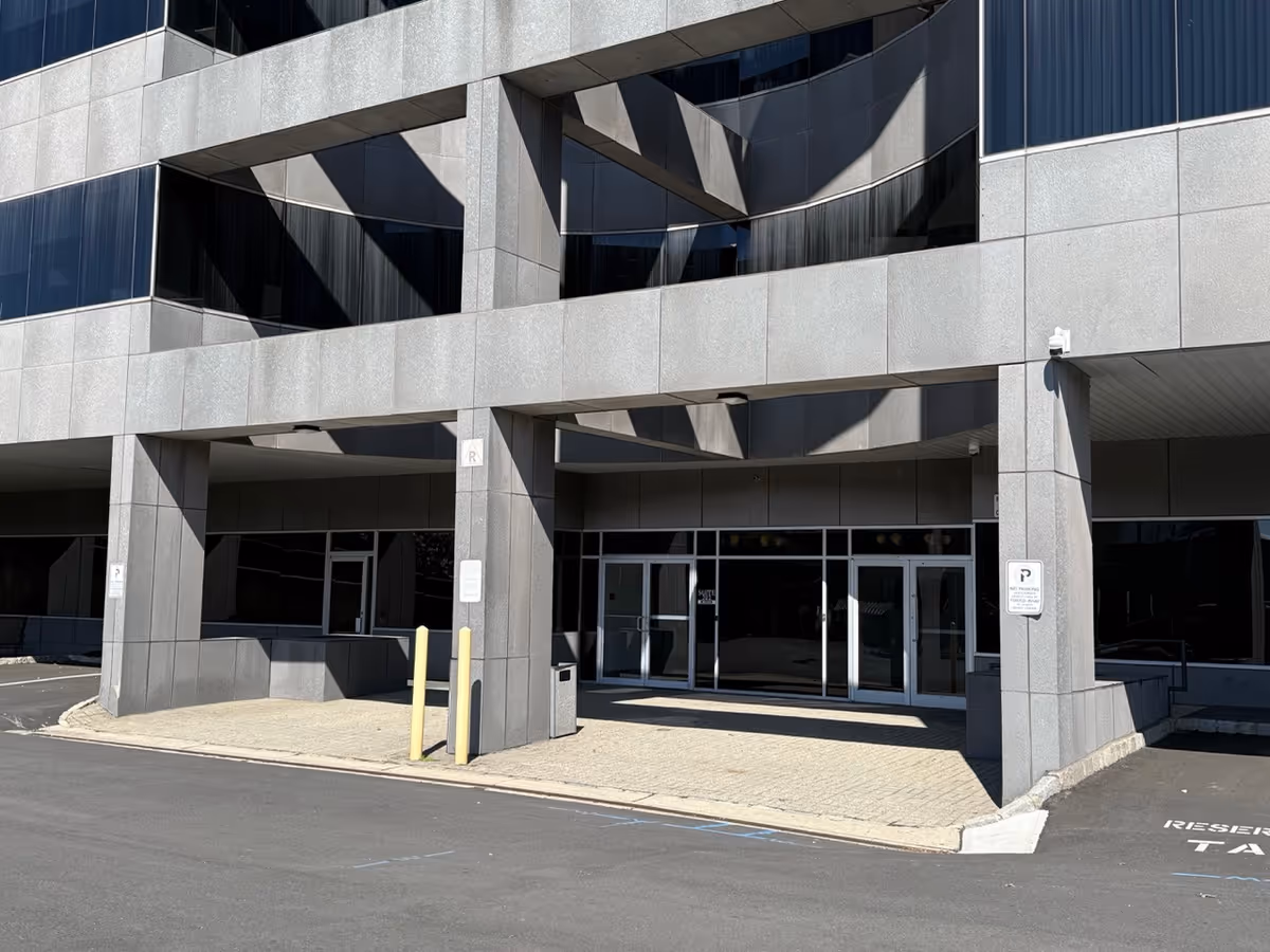 Modern gray building exterior featuring glass doors, pillars, and a wide entrance.