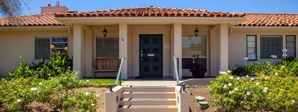 Front entrance of a single-story facility with steps, porch, and landscaped shrubs.