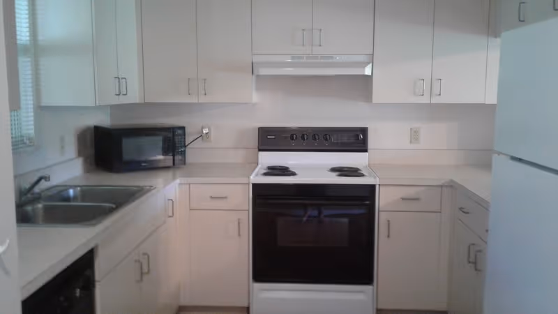 Compact kitchen with white cabinets, an electric stove/oven, microwave, sink, and refrigerator.