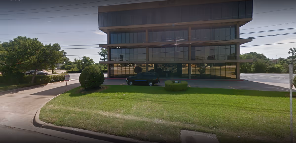 Modern glass-front commercial building with a manicured lawn and a small black vehicle in front.