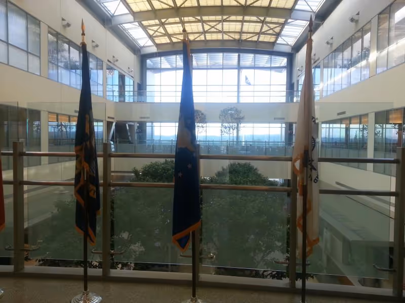 Bright atrium with flags on stands, glass railings, and skylights overlooking trees.