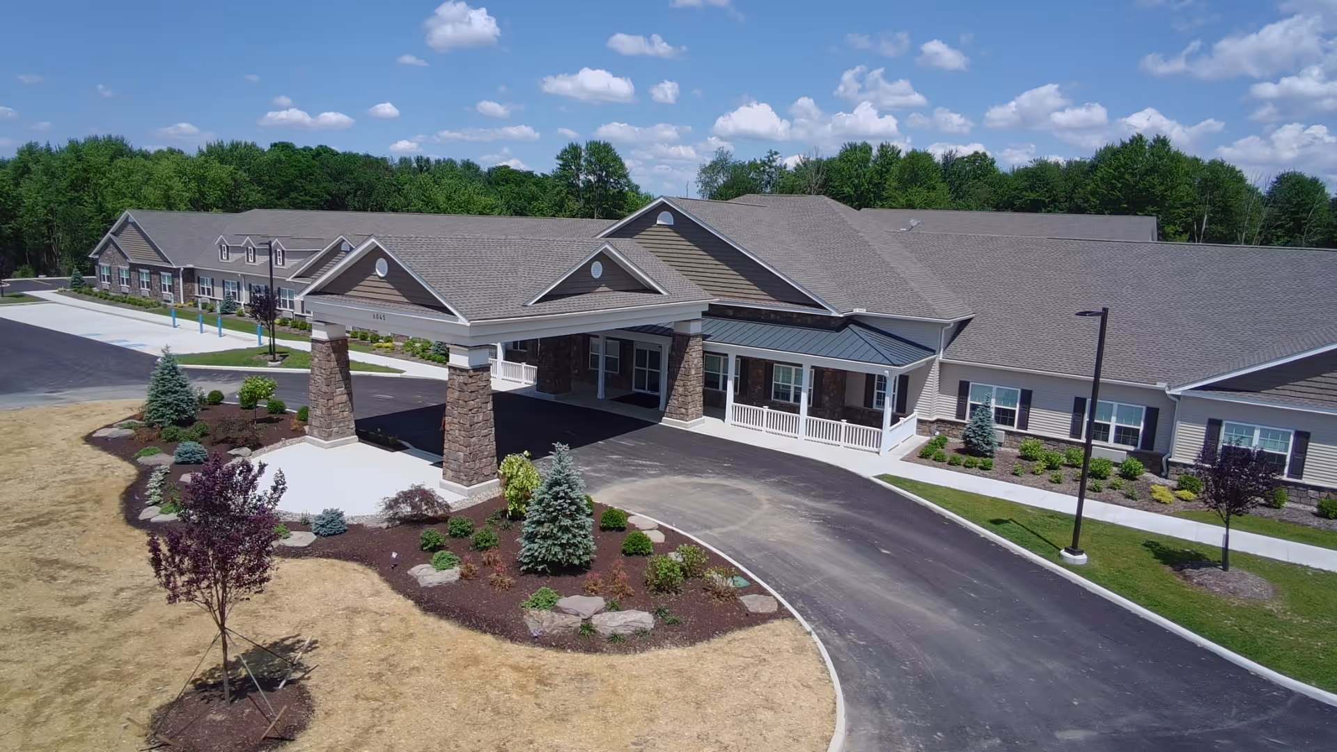 Exterior view of a single-story senior living facility with curved driveway and covered entrance.