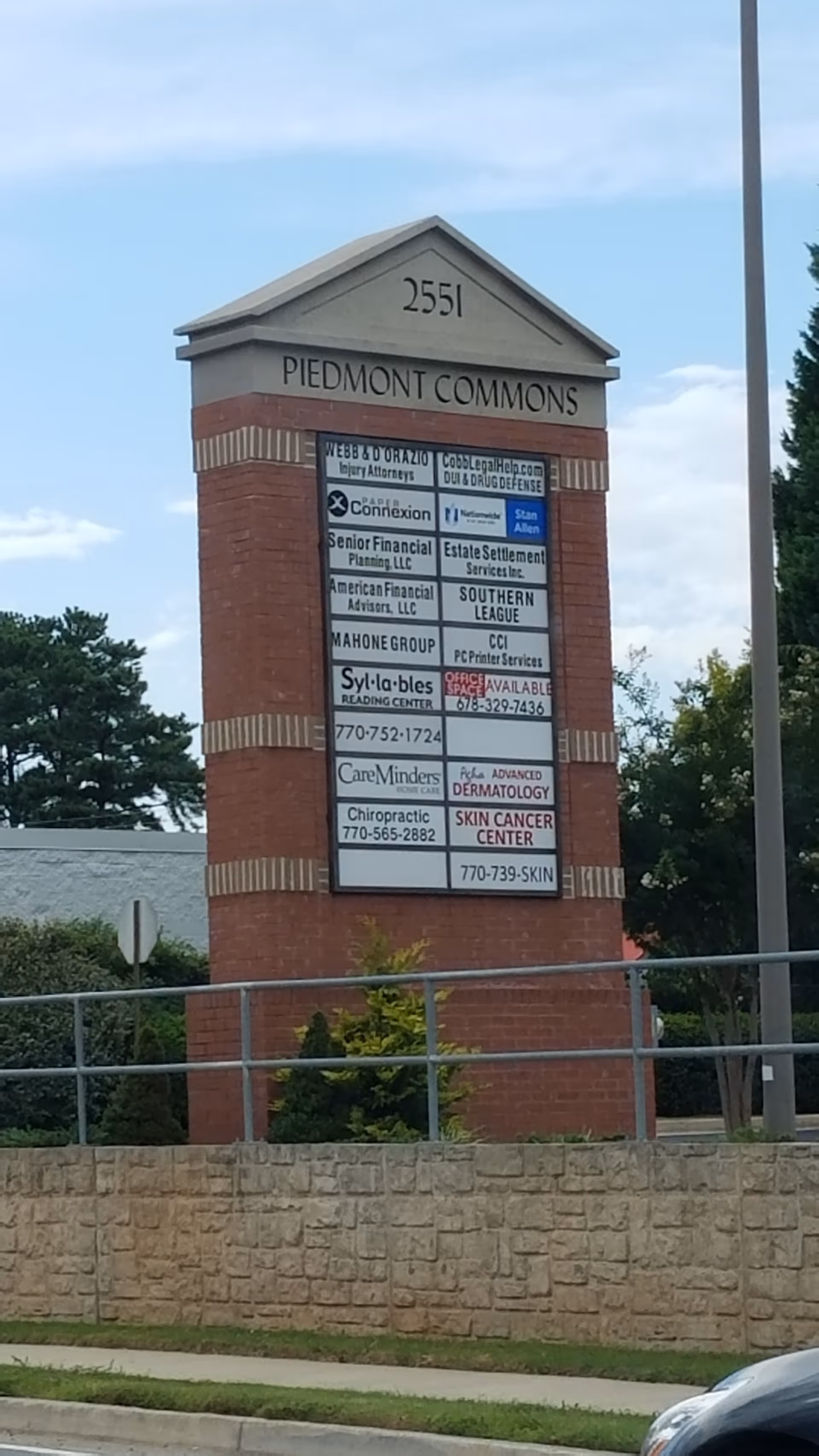 Brick sign tower listing tenants for Piedmont Commons beside a low stone wall.