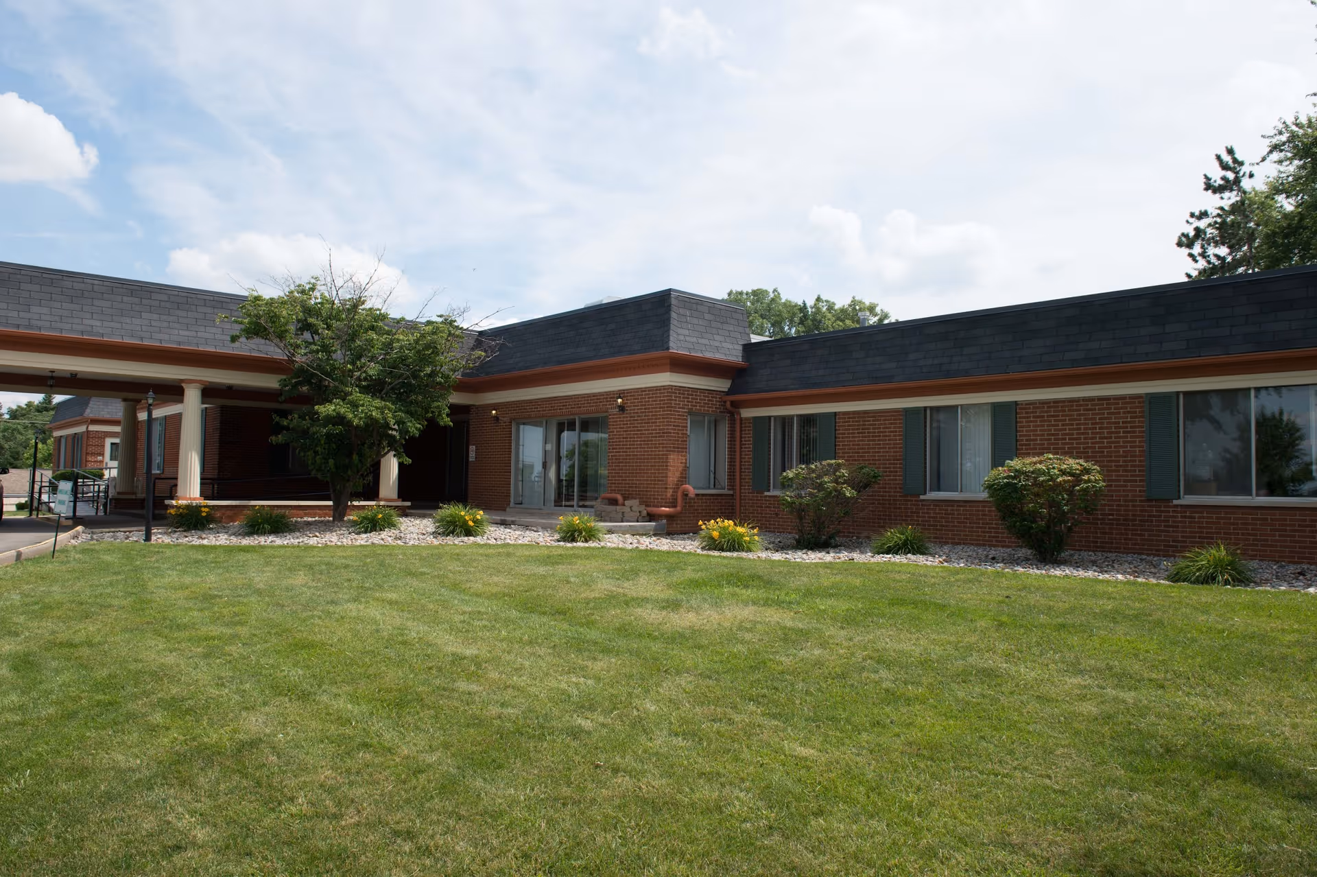 Brick, single-story senior care center exterior with landscaped lawn and entryway.