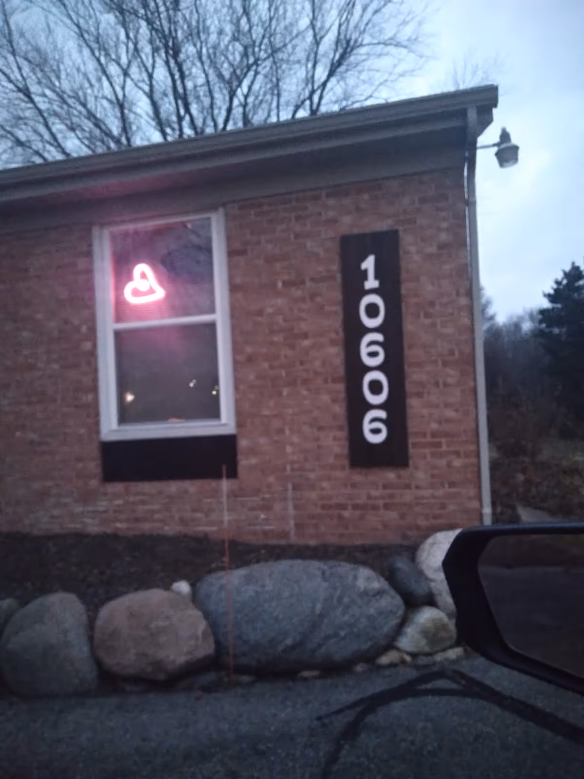 Brick building exterior with vertical address sign and pink neon heart visible in window.