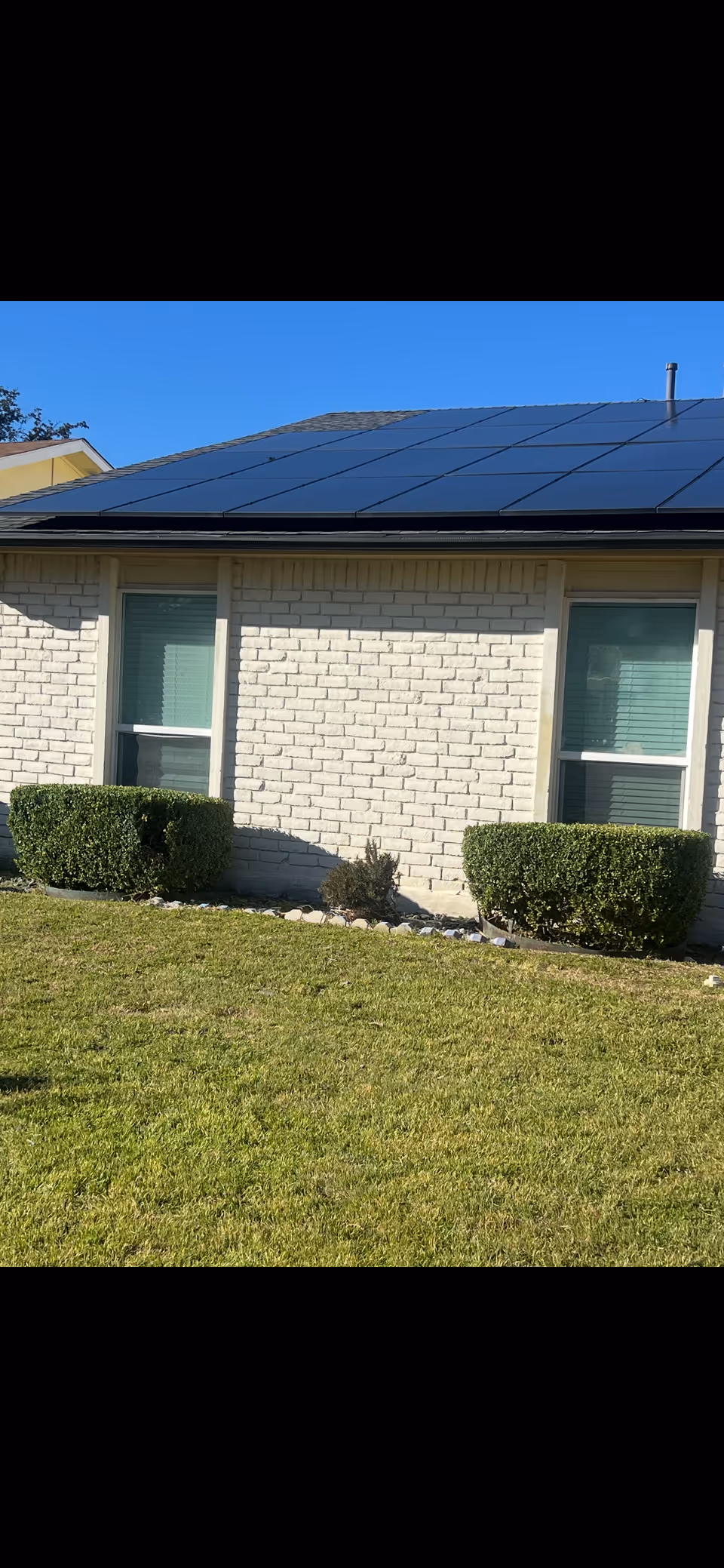 Exterior view of a care home with brick walls, shrubs, and solar panels on the roof.