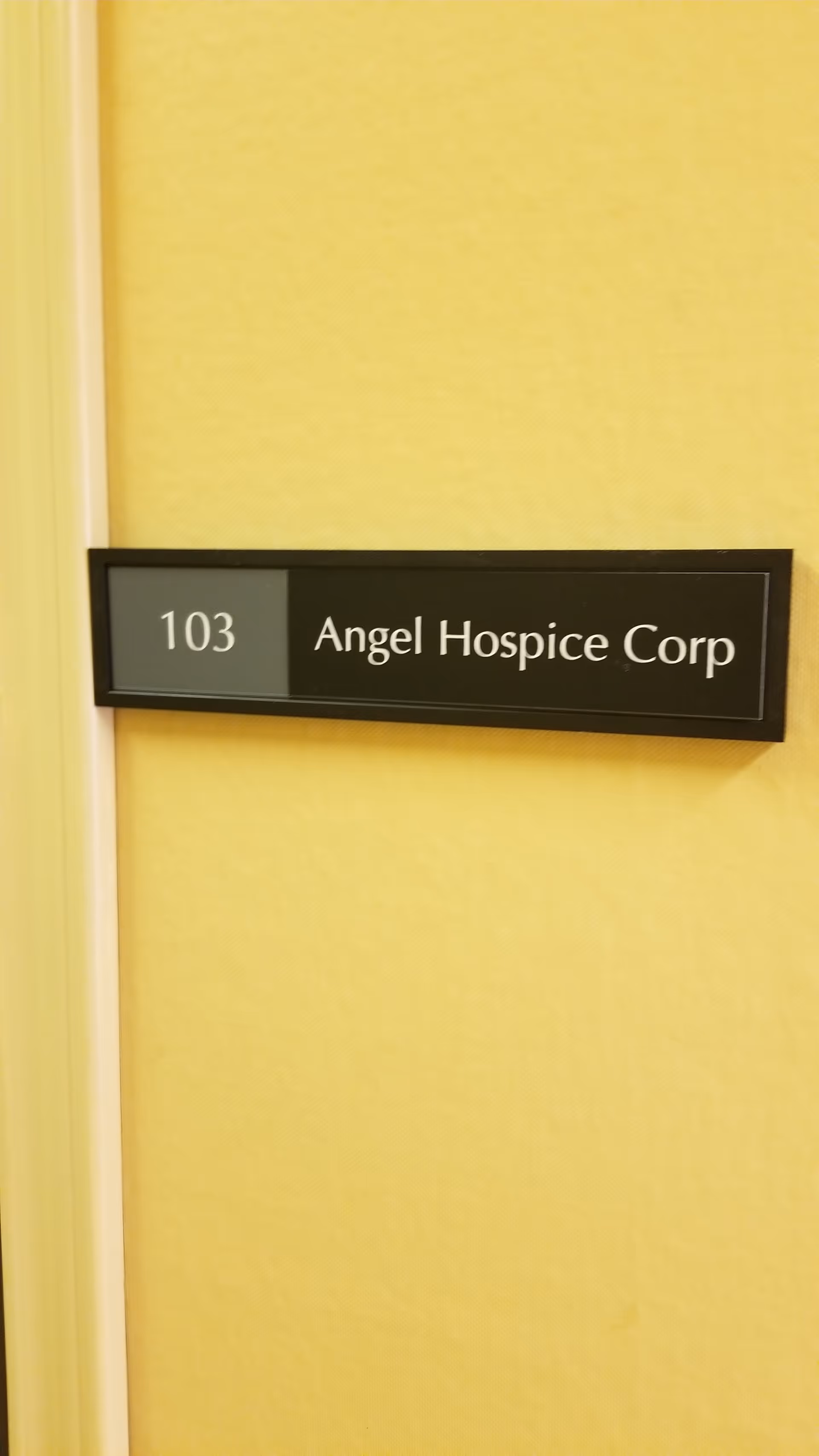 Interior wall with a doorway sign reading '103 Angel Hospice Corp' on yellow wallpaper.