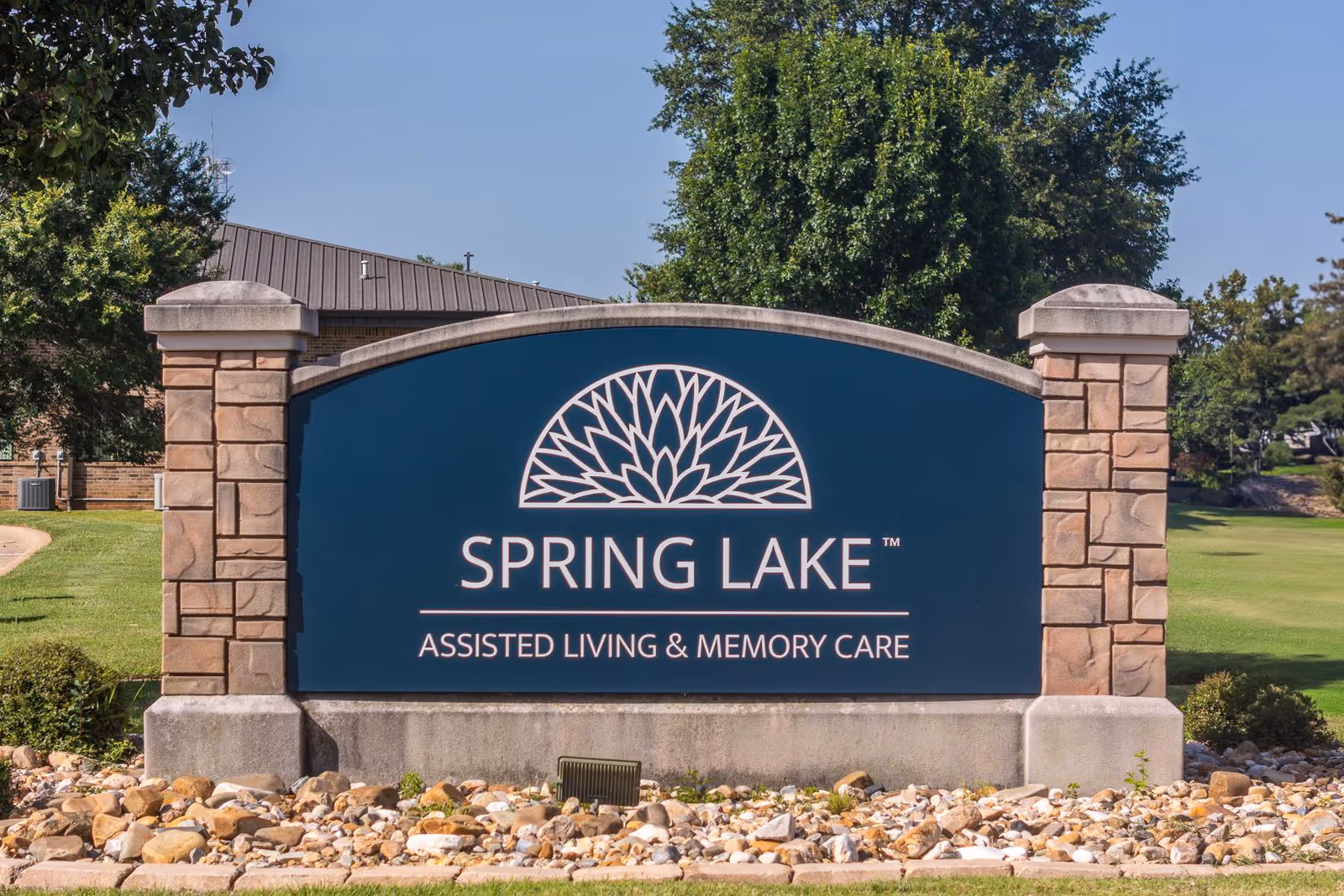 A blue Spring Lake sign with stone pillars in a landscaped outdoor area