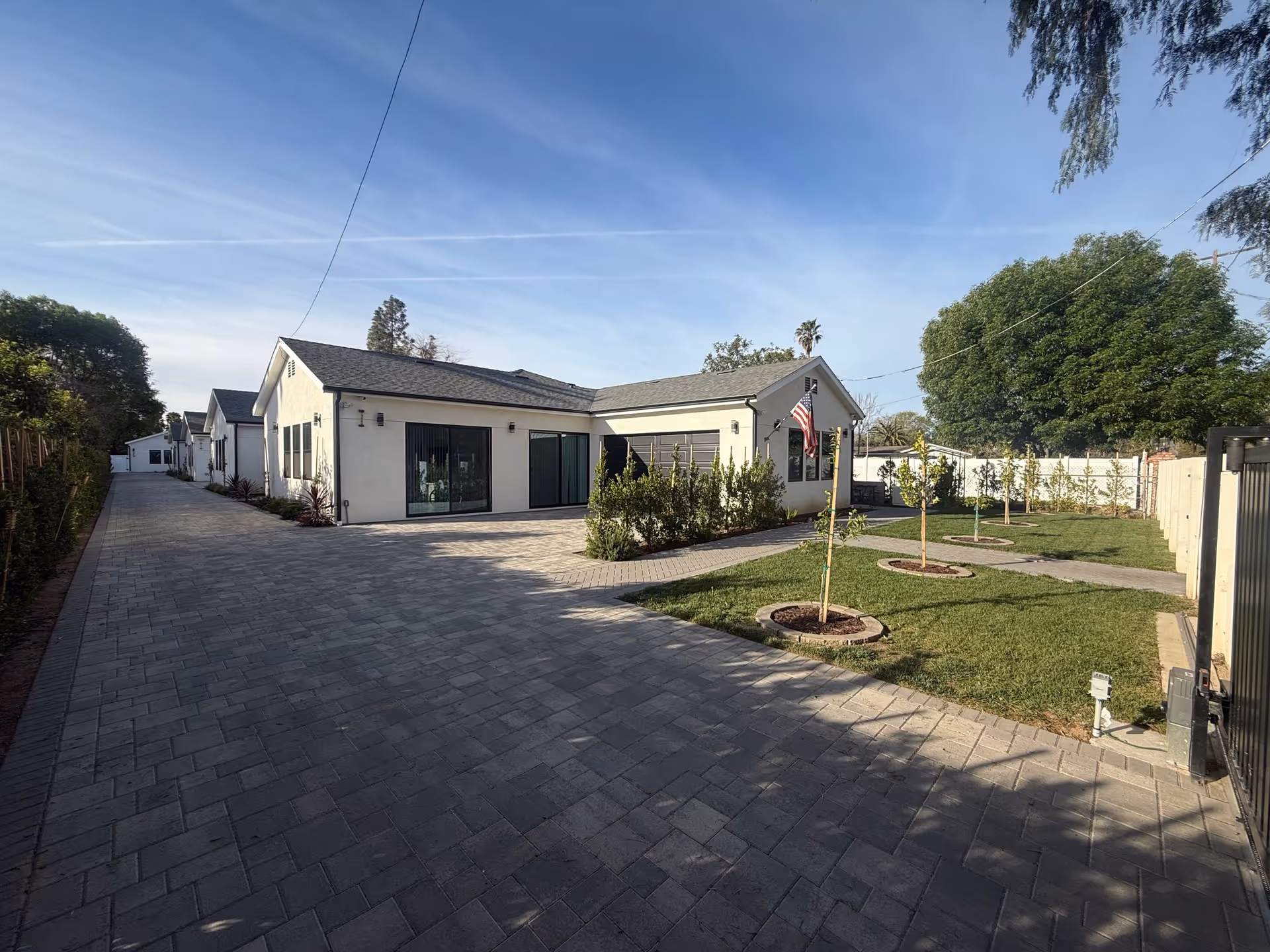 Single-story senior living facility exterior with a paved driveway, manicured lawn, trees, and an American flag.