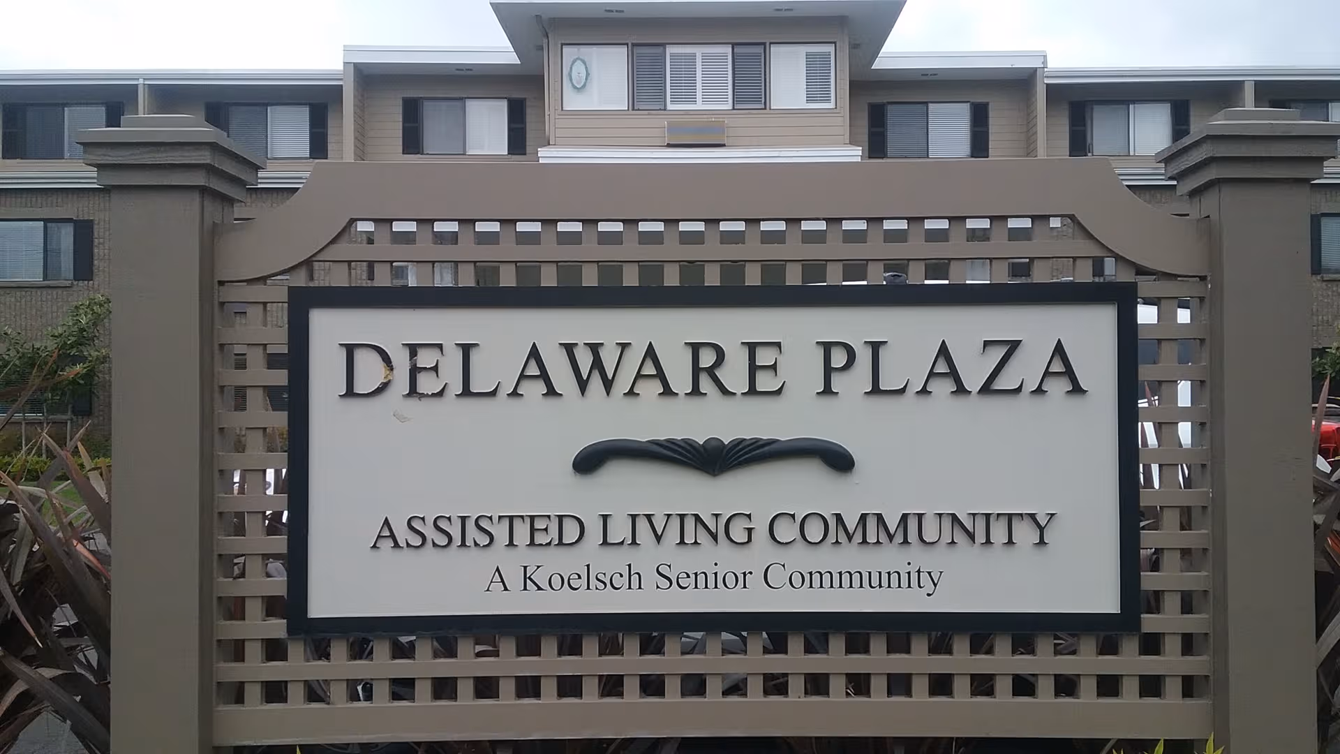 Front sign for Delaware Plaza Assisted Living Community with a multi-story building behind.