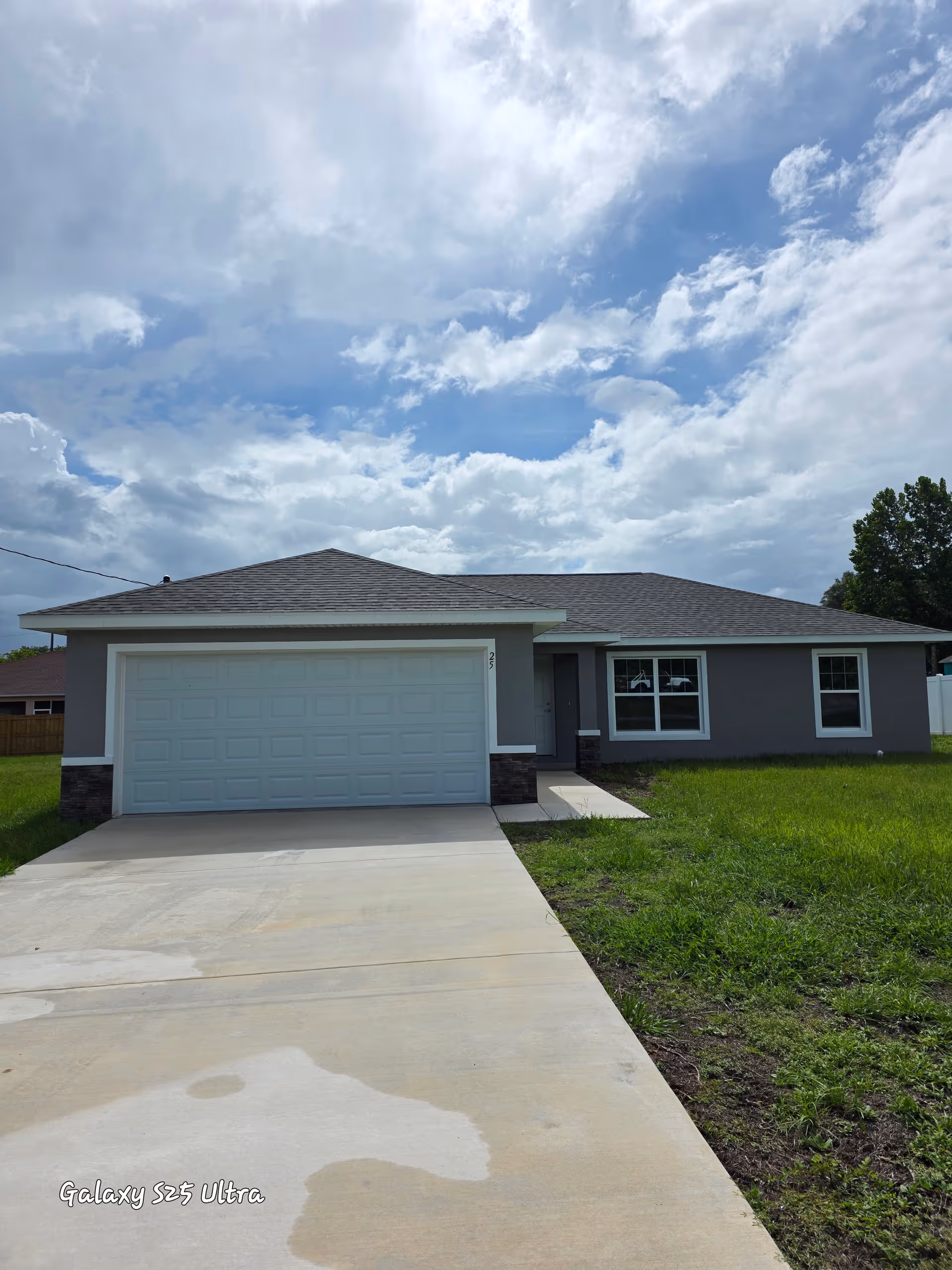 A single-story gray house with a two-car garage and front lawn under a cloudy sky.